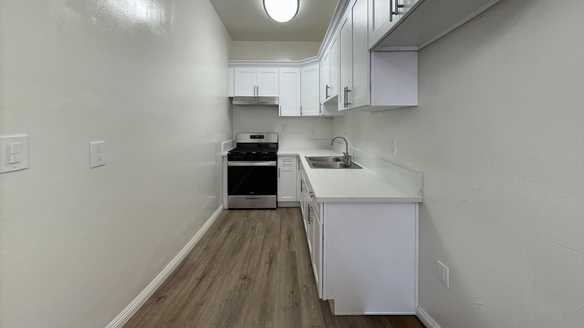 Small white kitchen with stove, cabinets, sink, and wood-look floor.