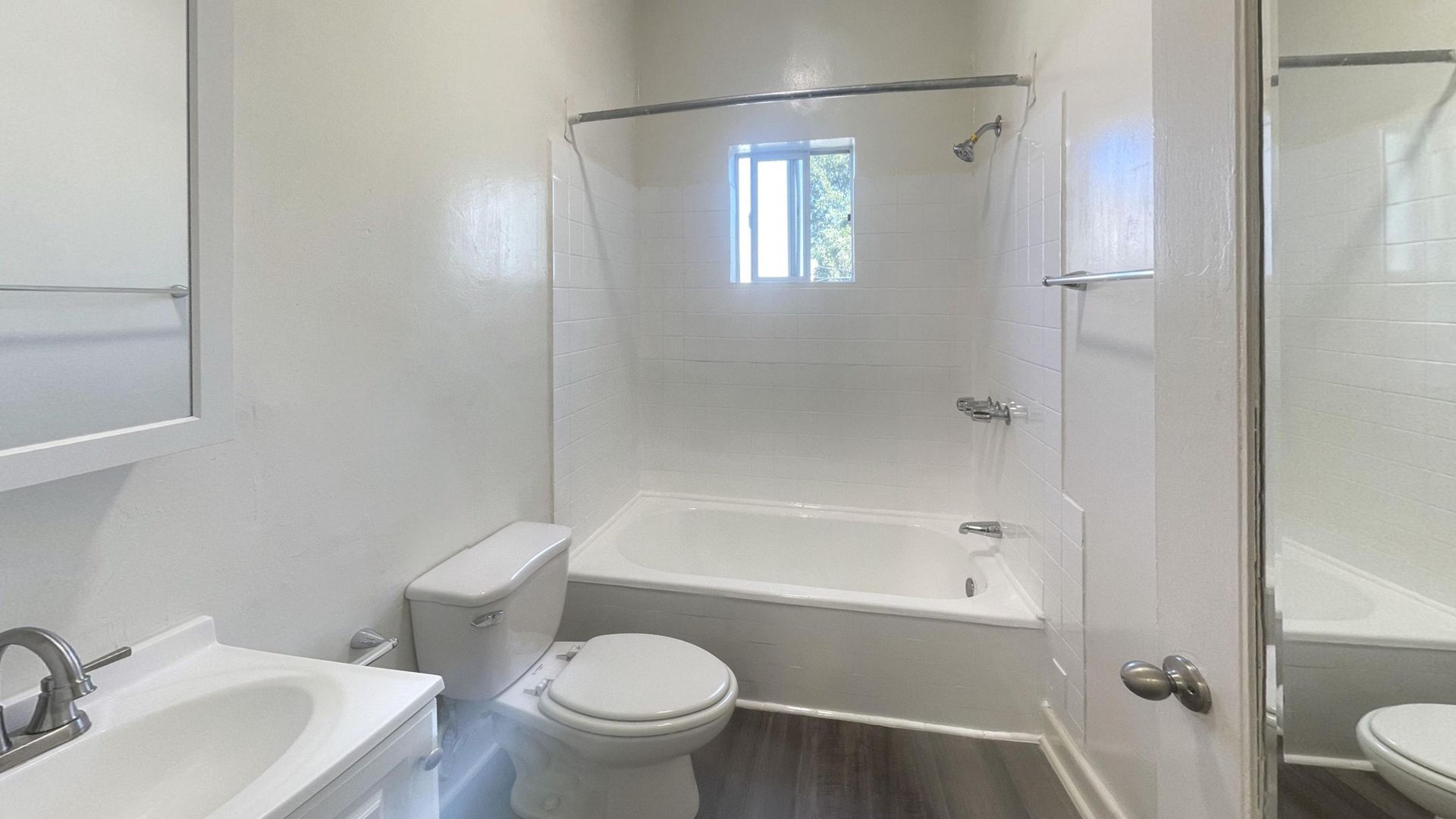 Bathroom with white walls, bathtub, toilet, sink, and window.