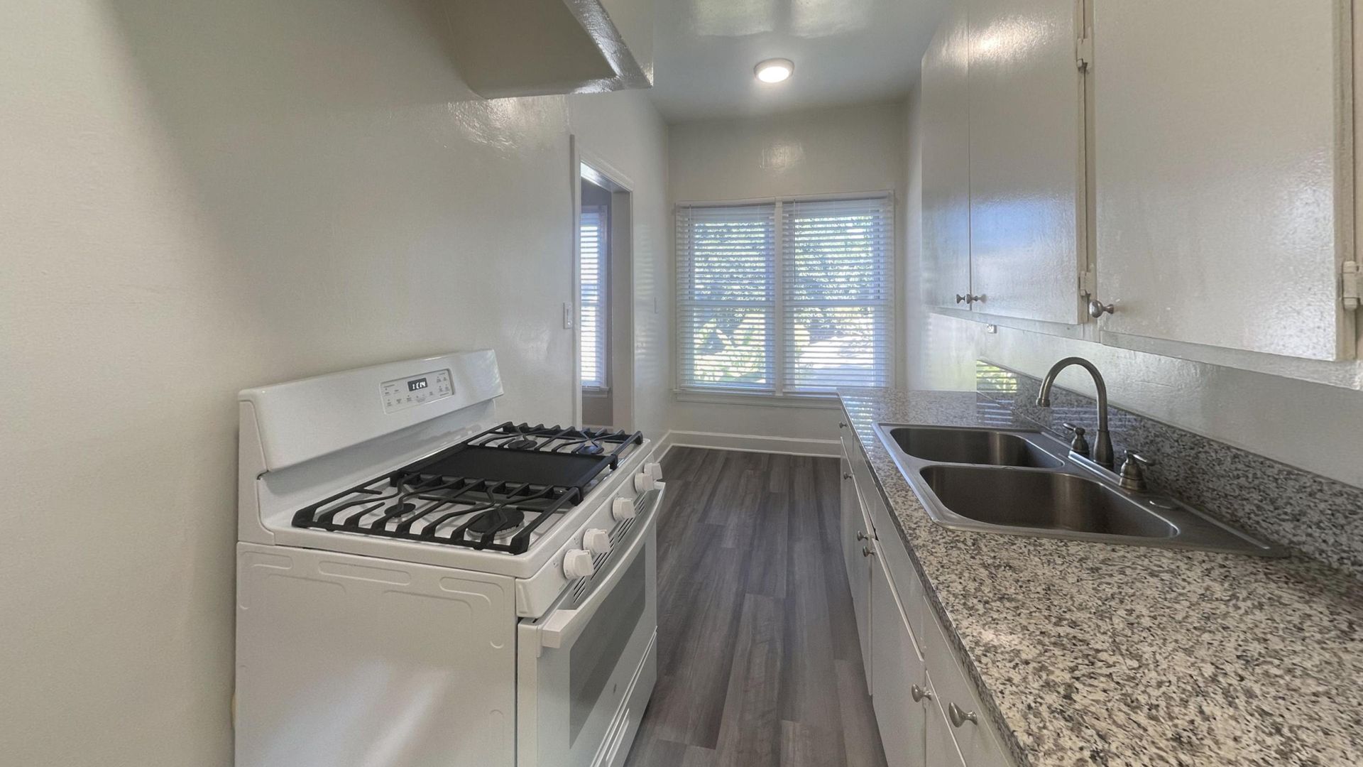 White kitchen with stove, sink, cabinets, window, and gray countertops.