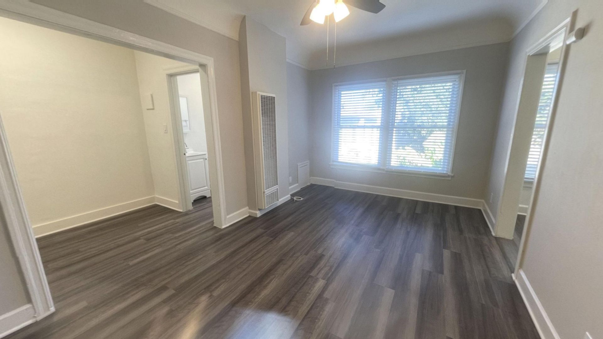 Empty room with dark wood-look flooring, two windows, doorway to bathroom and another doorway.