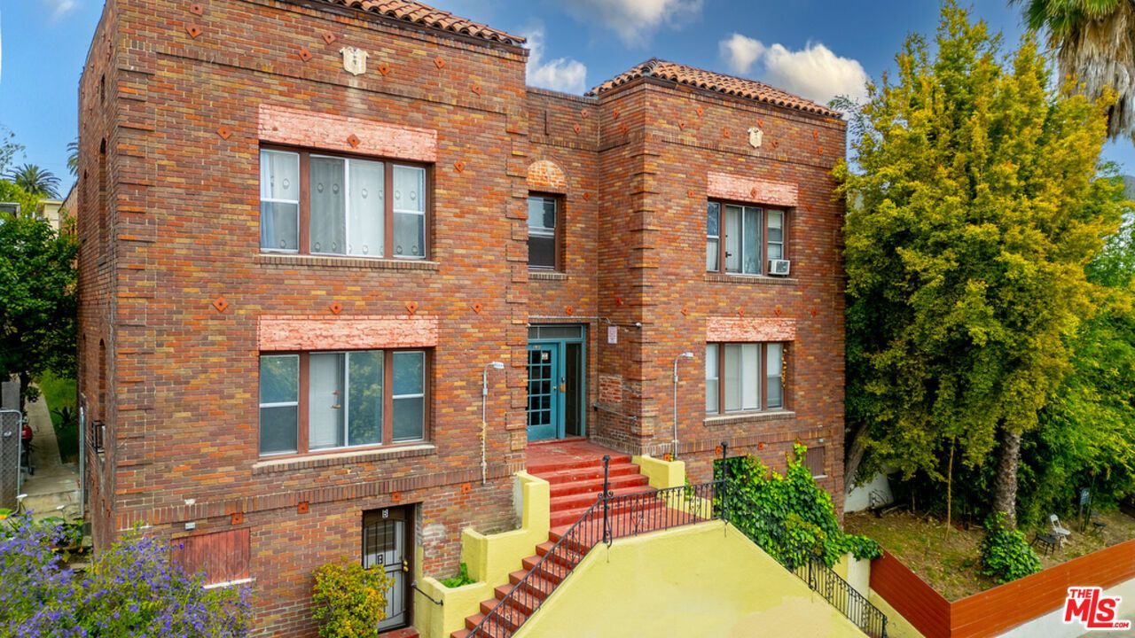 Two-story brick apartment building with red stairs and teal door.