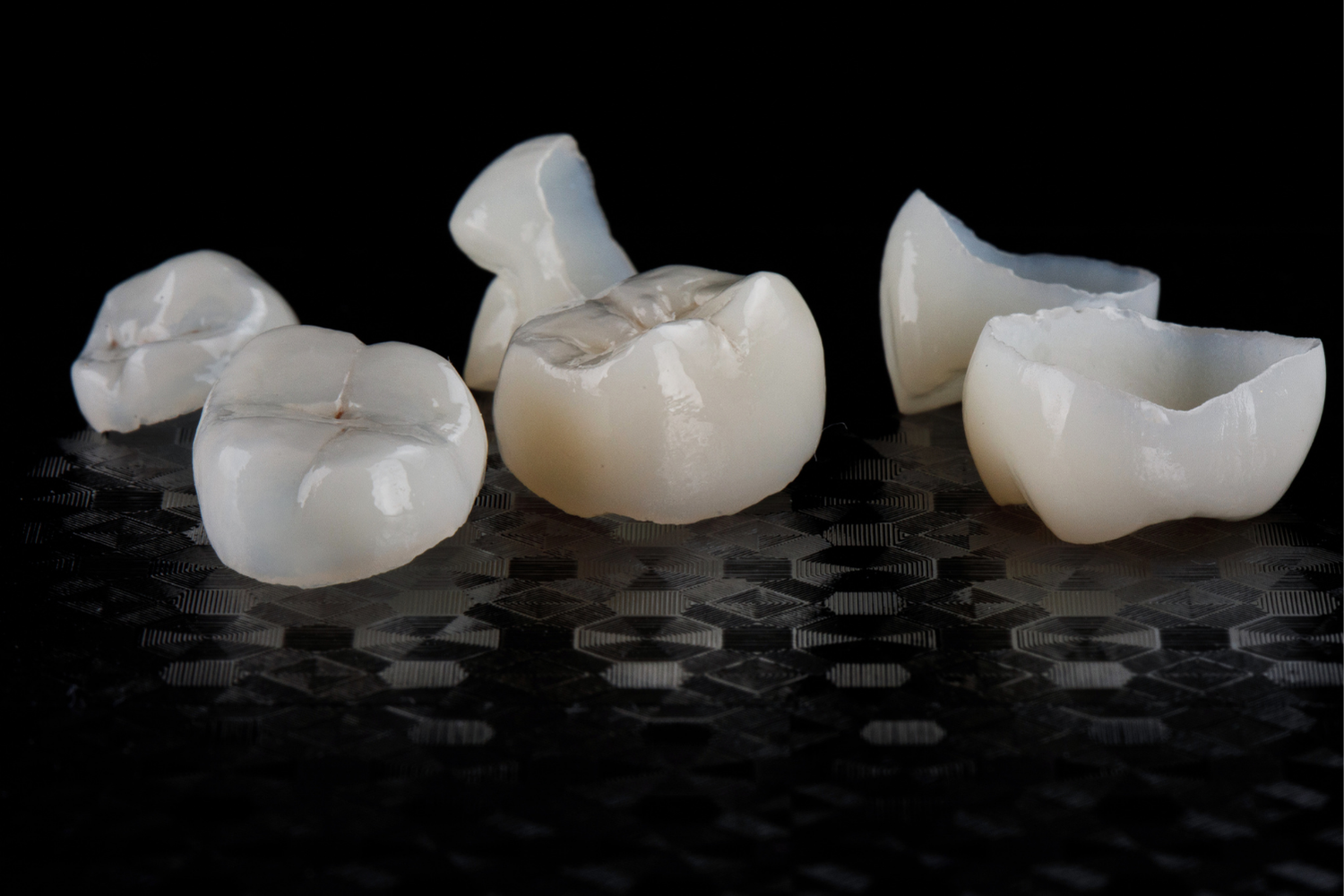 Several white, translucent dental crowns arranged on a dark, reflective, textured surface.