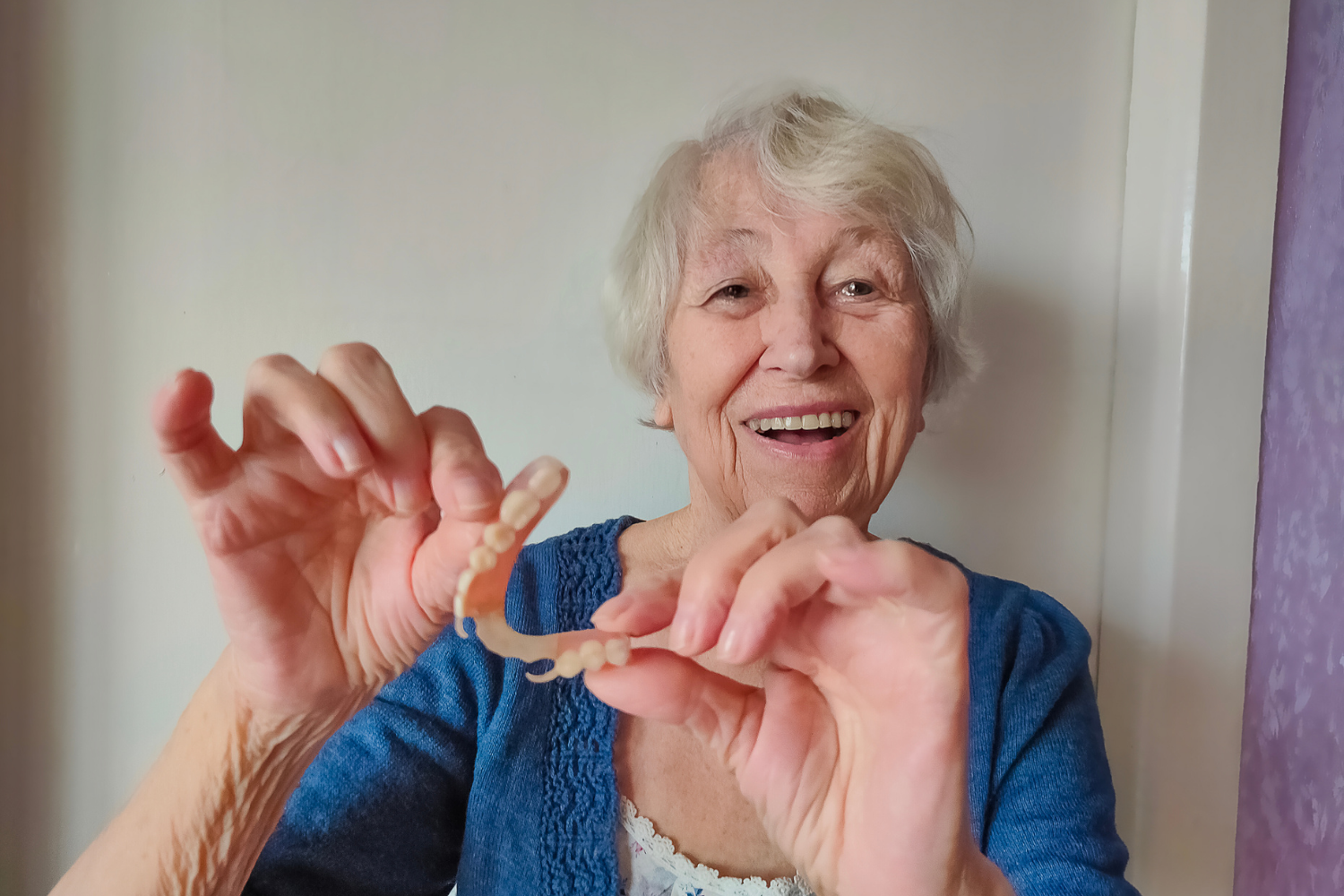 A person smiling while holding a clear, flexible dental appliance in their hands.