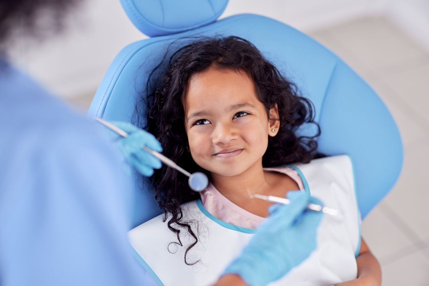 A person sitting in a dental chair, smiling at a professional wearing blue medical gloves and holding dental tools.
