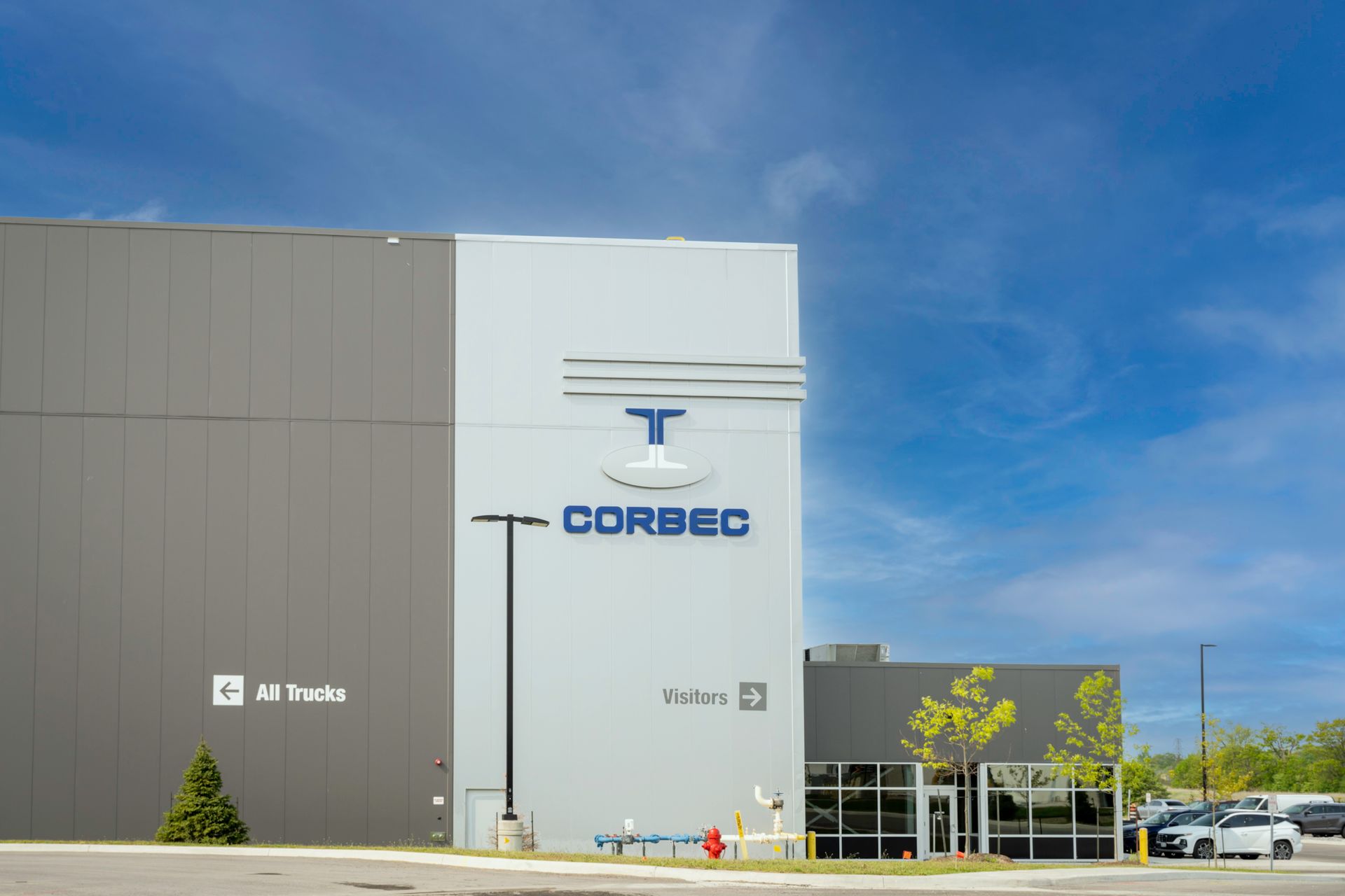 Exterior view of the Corbec building with blue logo on a grey wall under a blue sky.