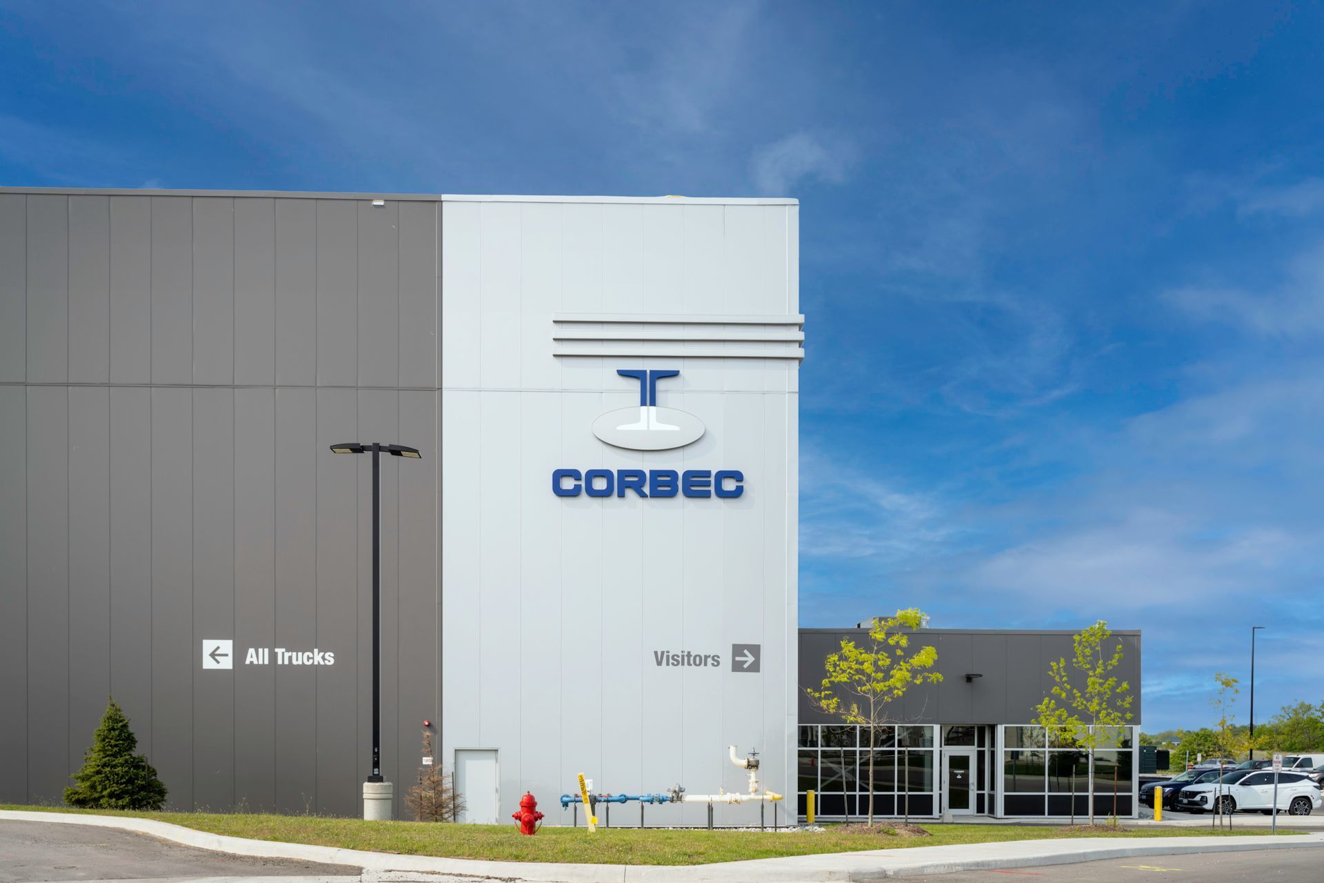 Exterior view of the Corbec building with blue logo on a grey and white building under a blue sky.
