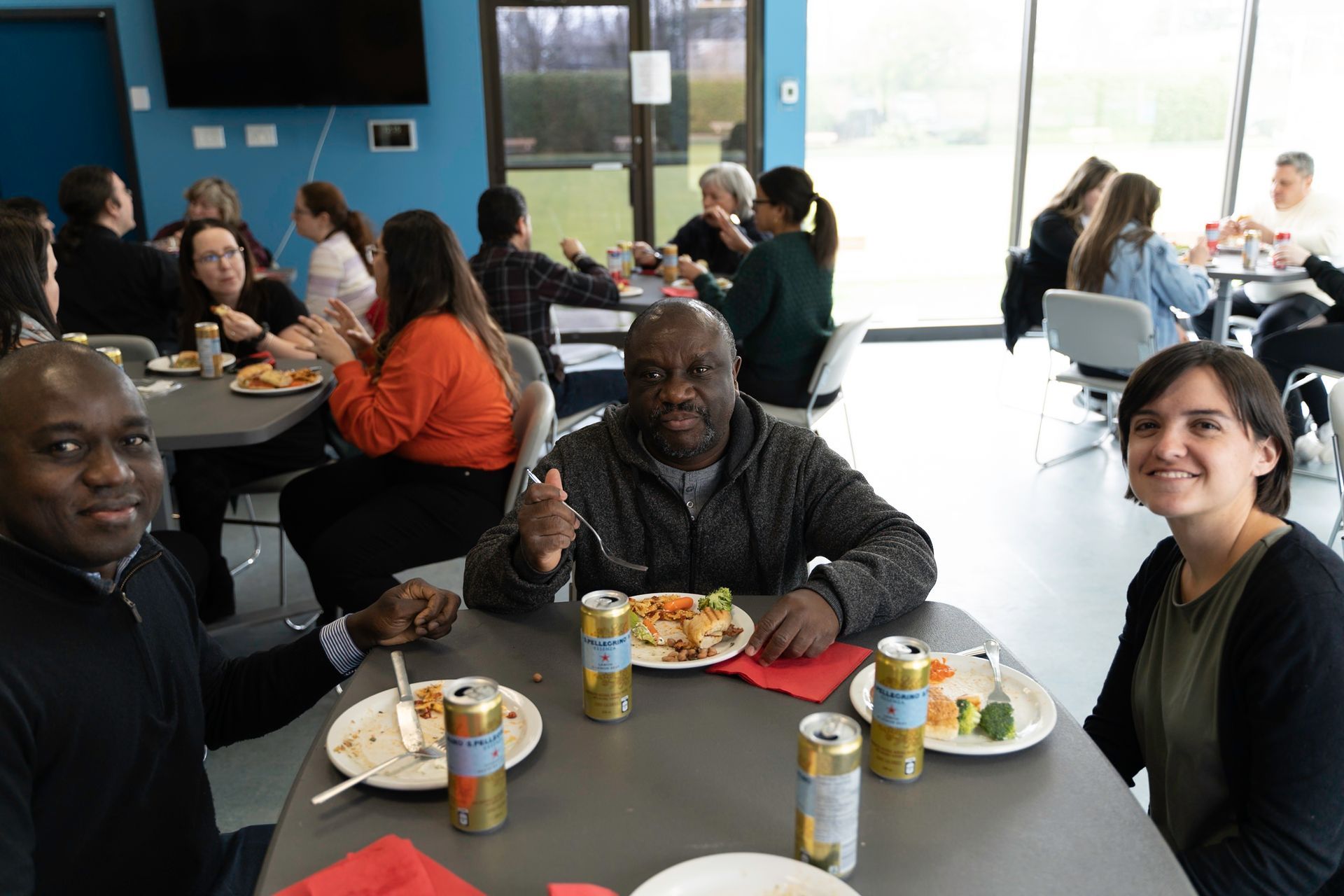 People eating lunch at tables in a cafeteria. Some smile and look at the camera.