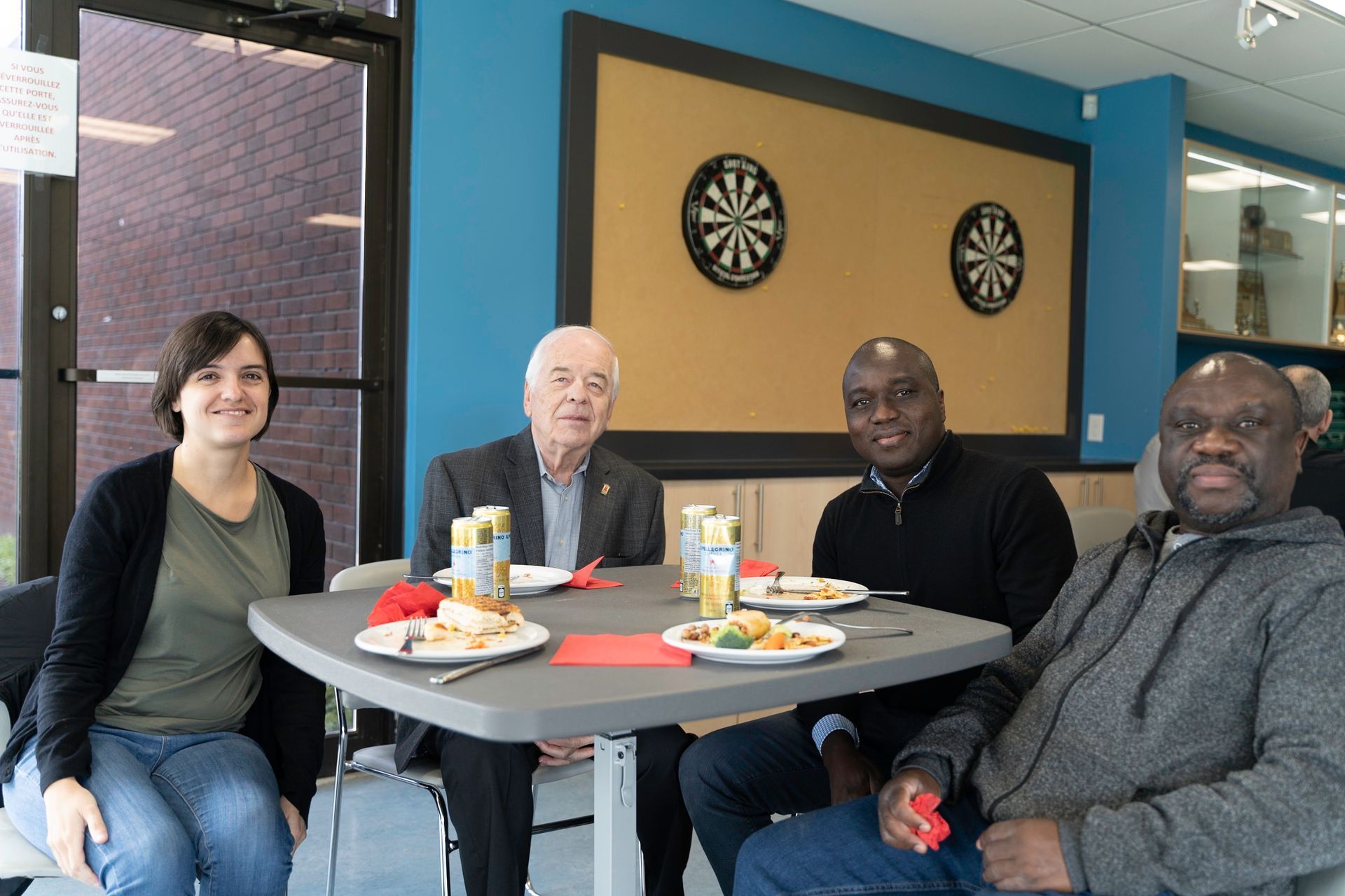 Four people seated around a table, eating. Blue wall with dart boards in the background.