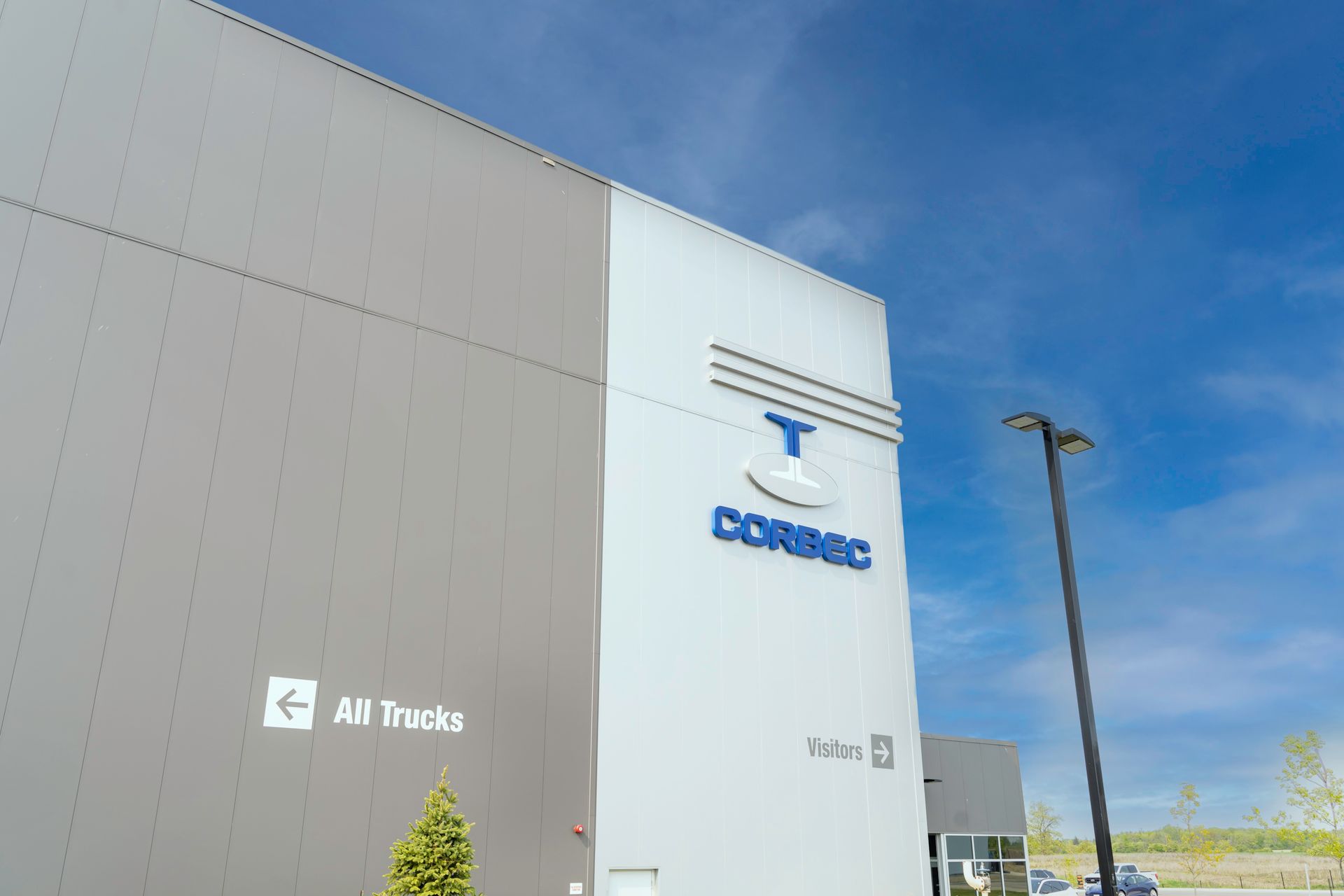 Exterior of a gray and white CORBEC building under a blue sky, with the company logo.