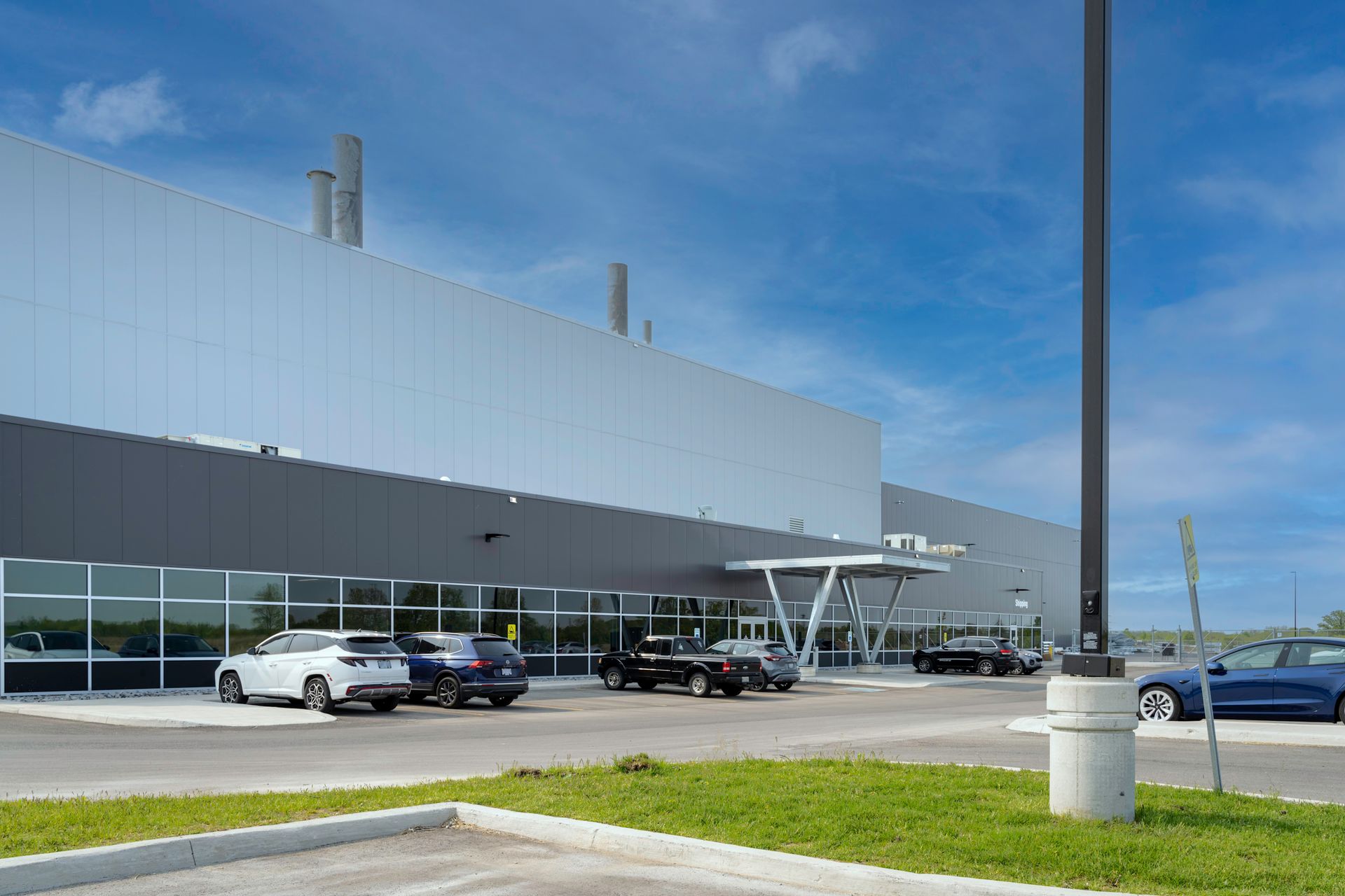 Modern industrial building exterior with cars parked out front, under a blue sky.