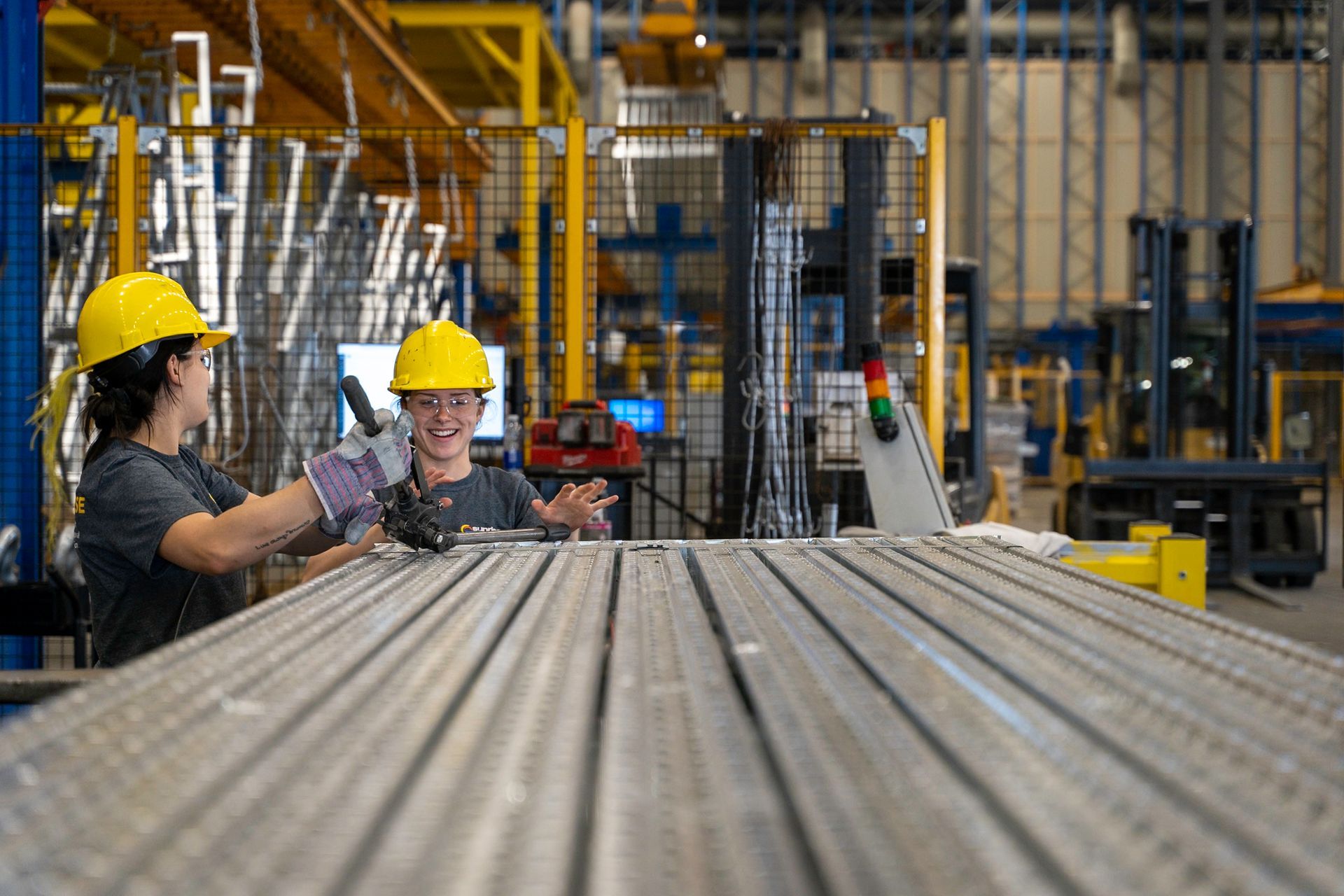 Two people in hard hats work with metal in a factory.