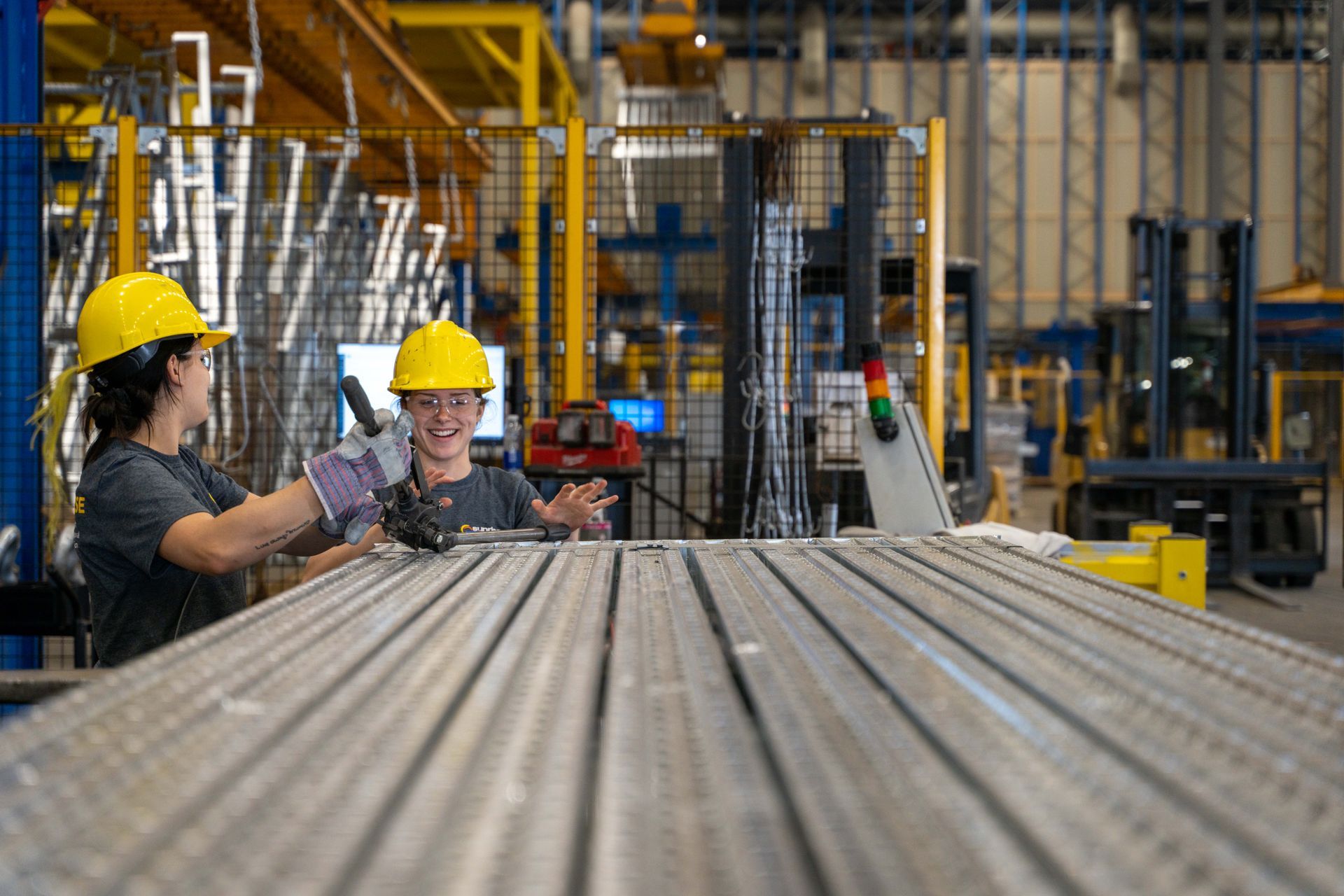 Two people in yellow hard hats working with metal in a factory setting.