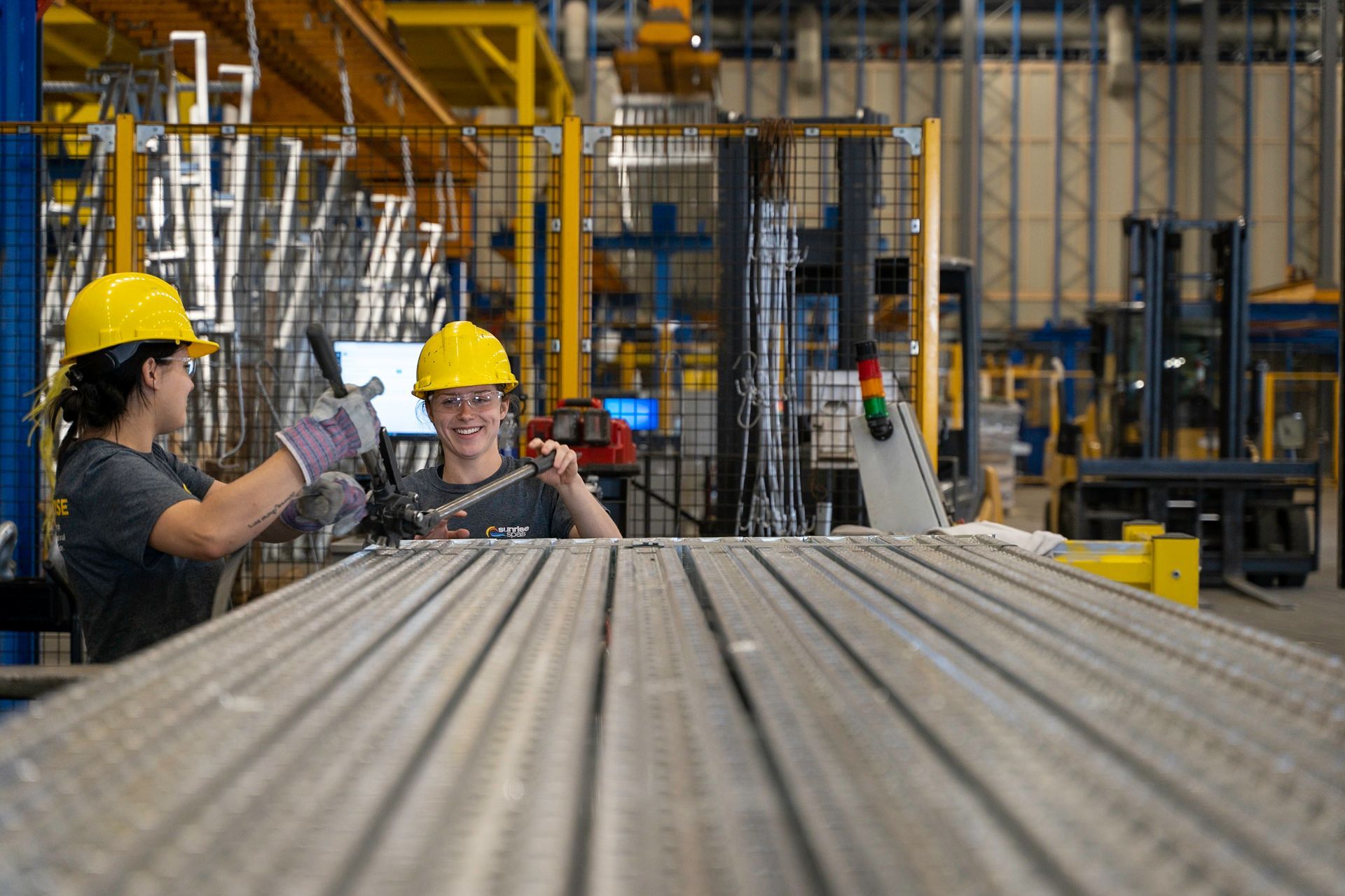 Two workers in yellow hard hats in a factory. They are working on a metal structure.