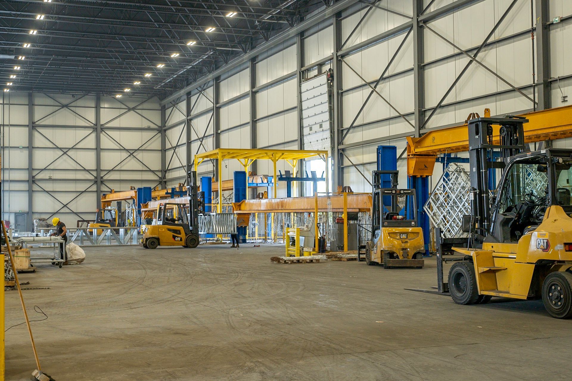 Warehouse interior with yellow forklifts and metal beams; workers moving materials.