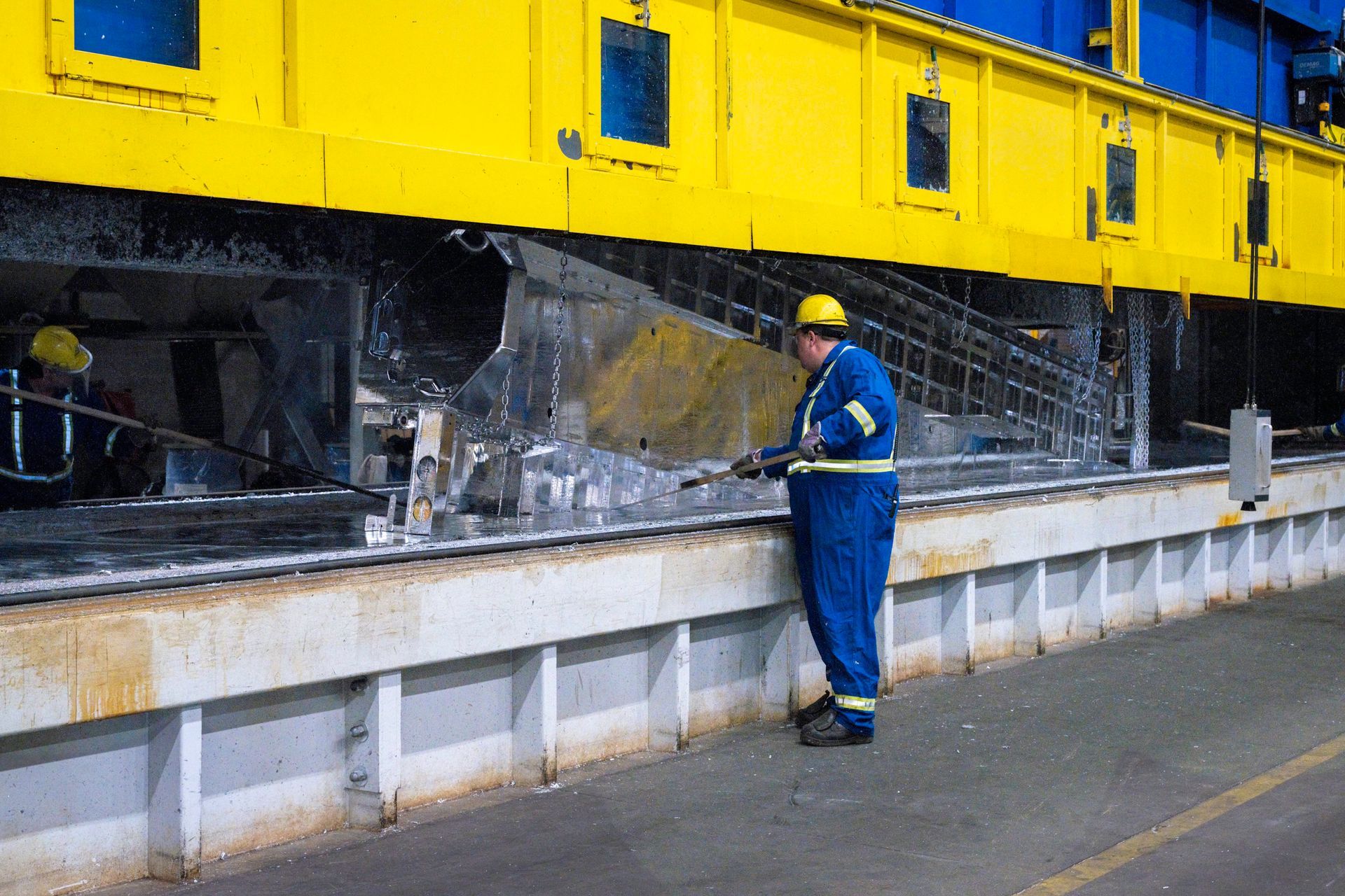Man in blue coveralls and hard hat inspects machinery at a factory.