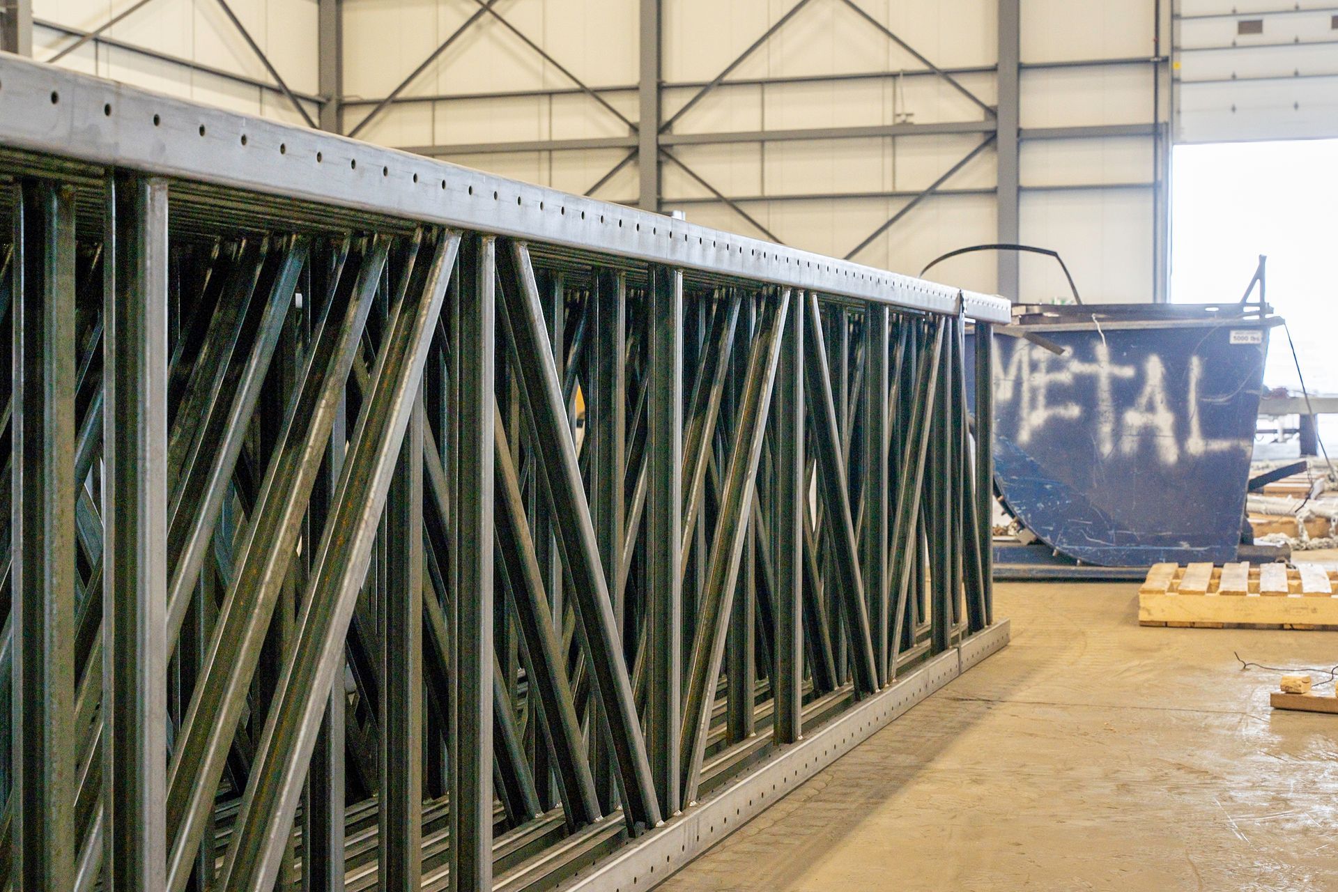 Metal truss sections stacked inside a warehouse, with 