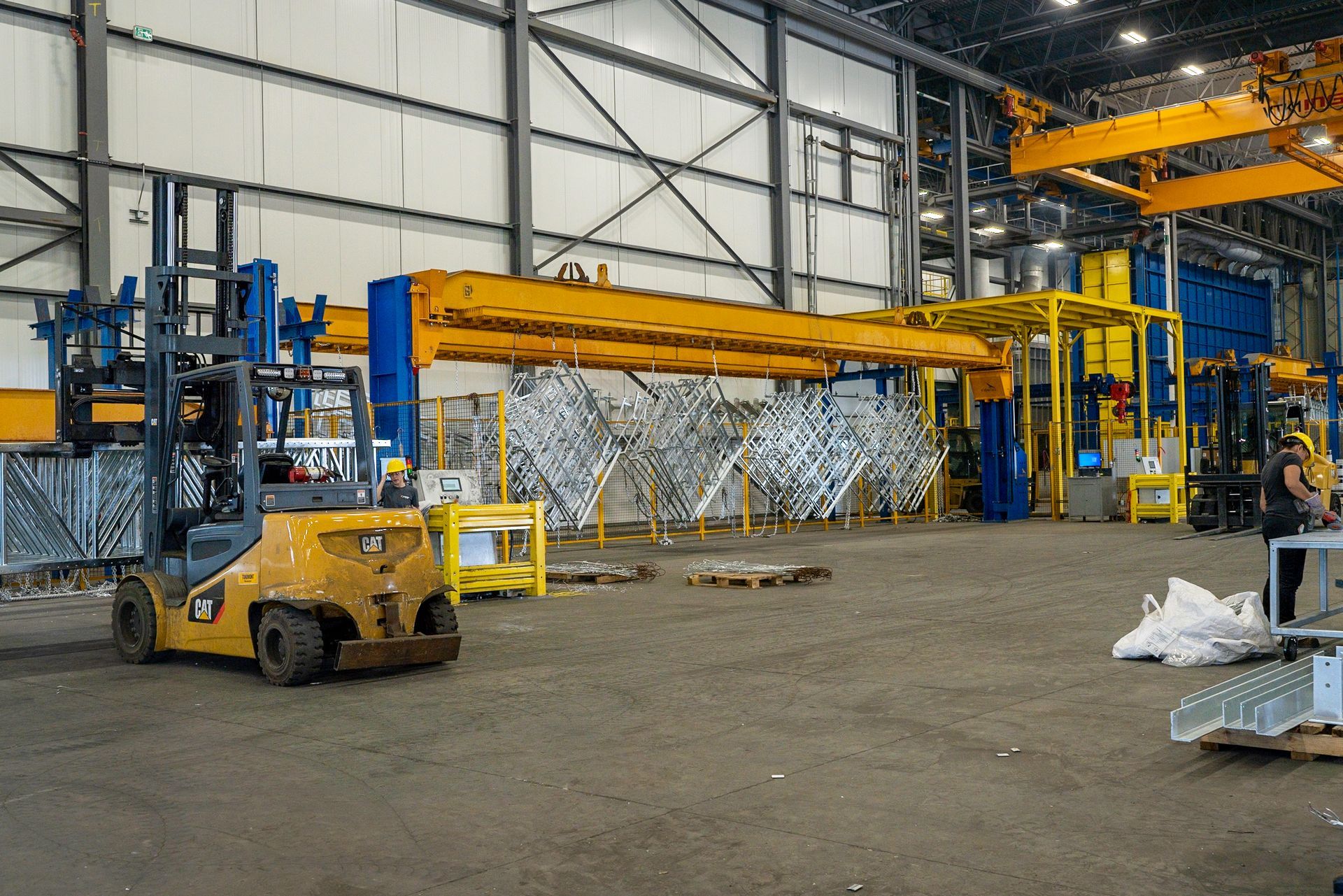 Forklift in a factory setting, moving metal parts near an overhead crane system.