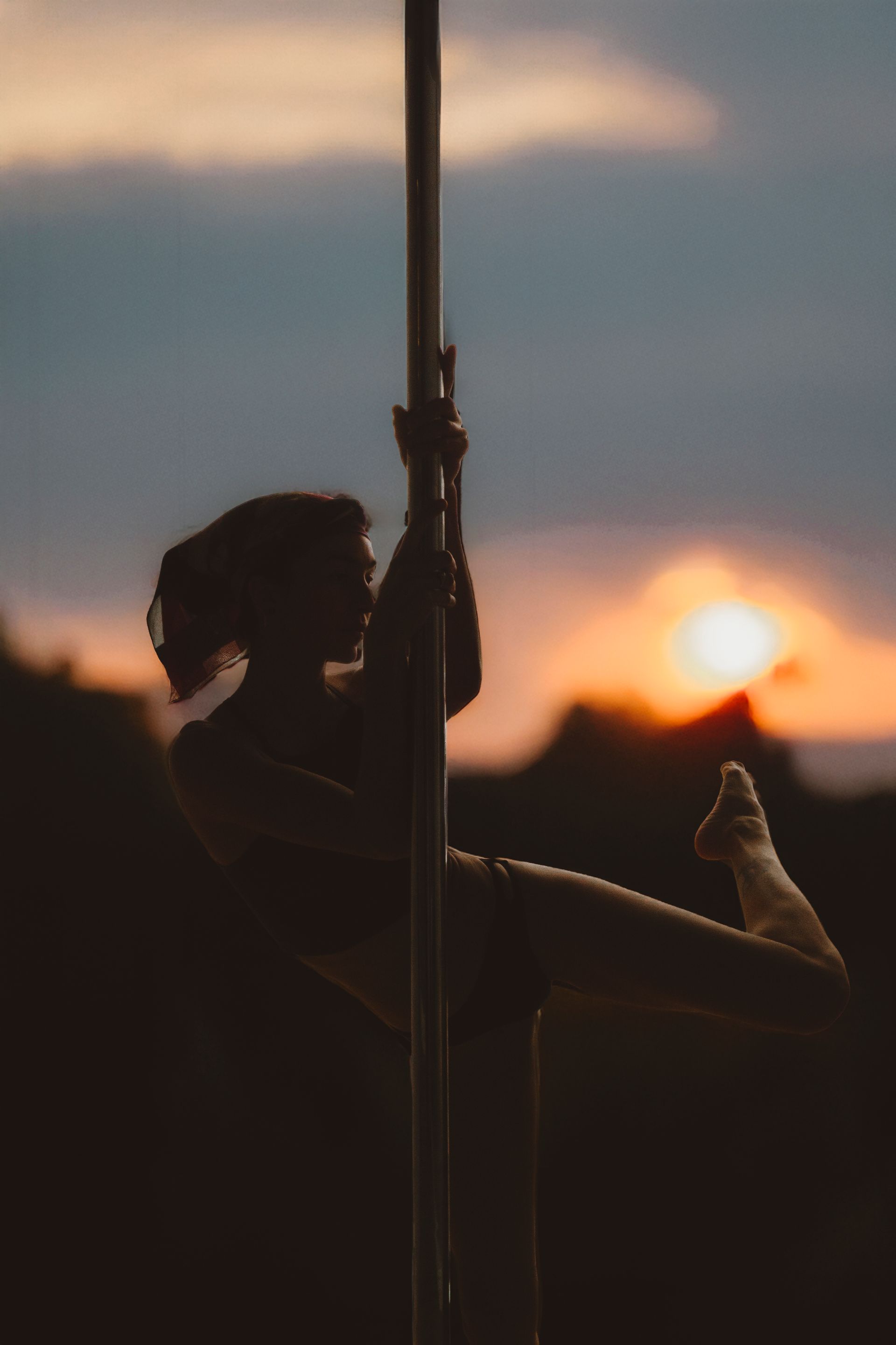 A silhouette of a person performing a pole dance move against a sunset sky.