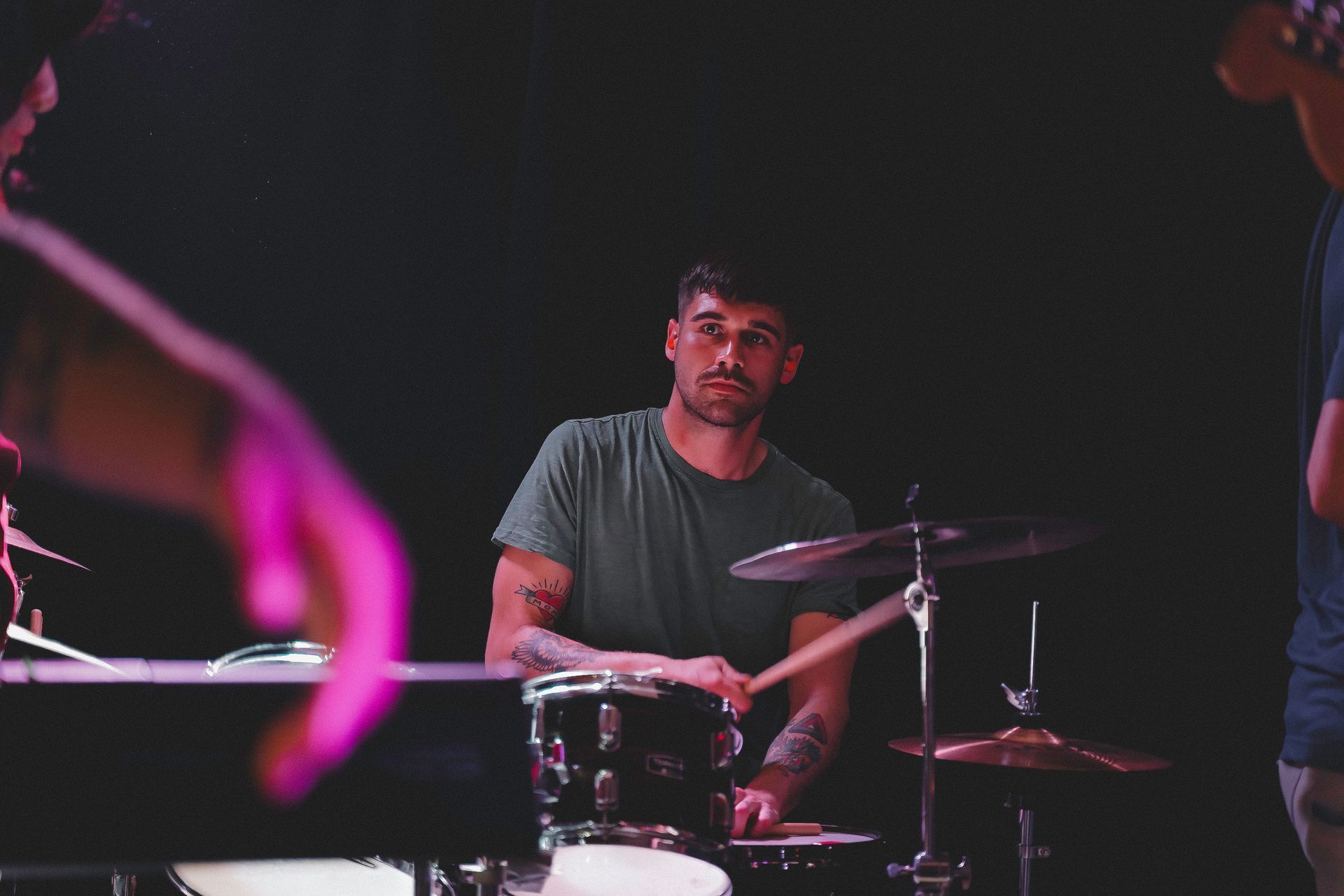 Drummer playing with a band, lit by stage lights.