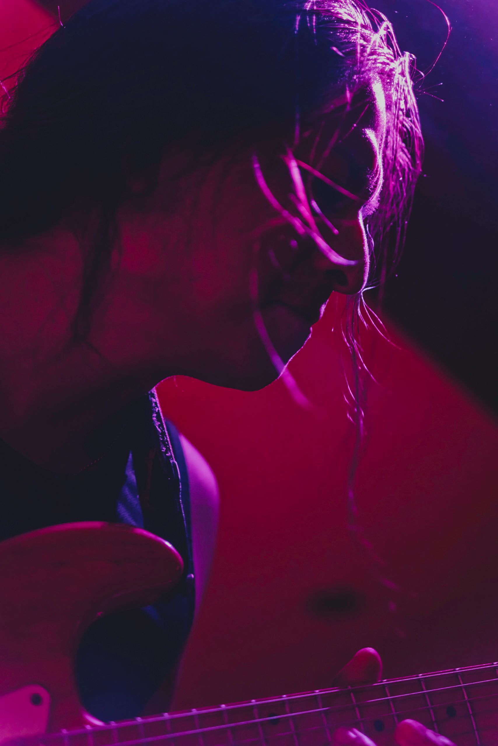 Guitarist plays electric guitar under magenta stage lighting.