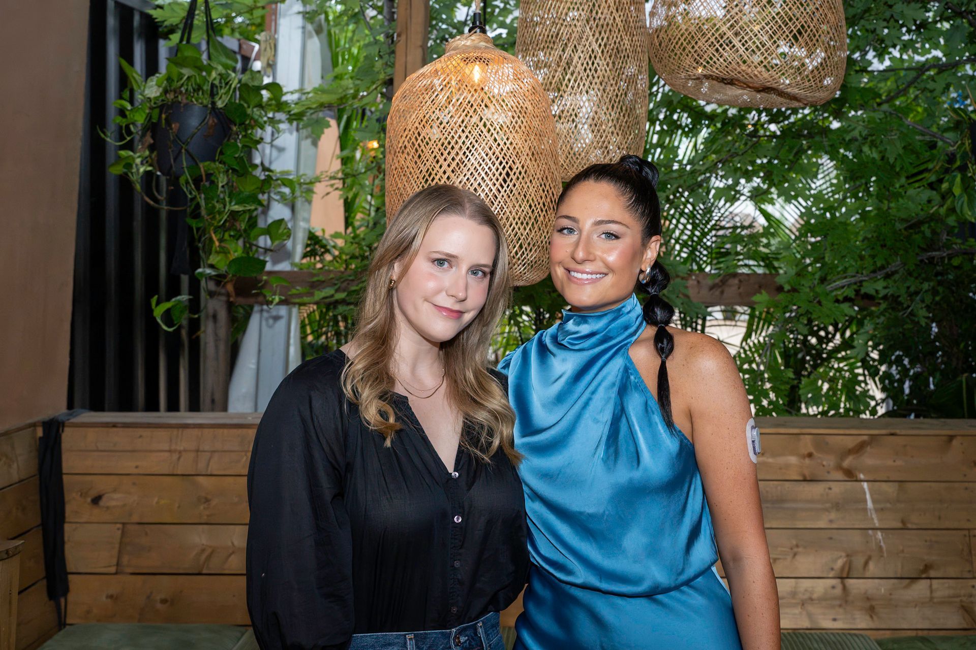 Two women smiling, posing for a photo in a restaurant. One wears blue; the other, black.
