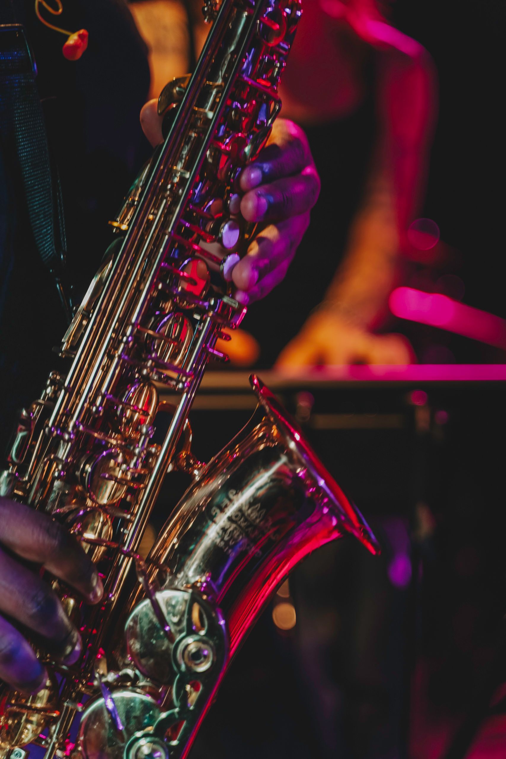 Close-up of a person's hands playing a shiny brass saxophone on stage, with colored stage lighting.