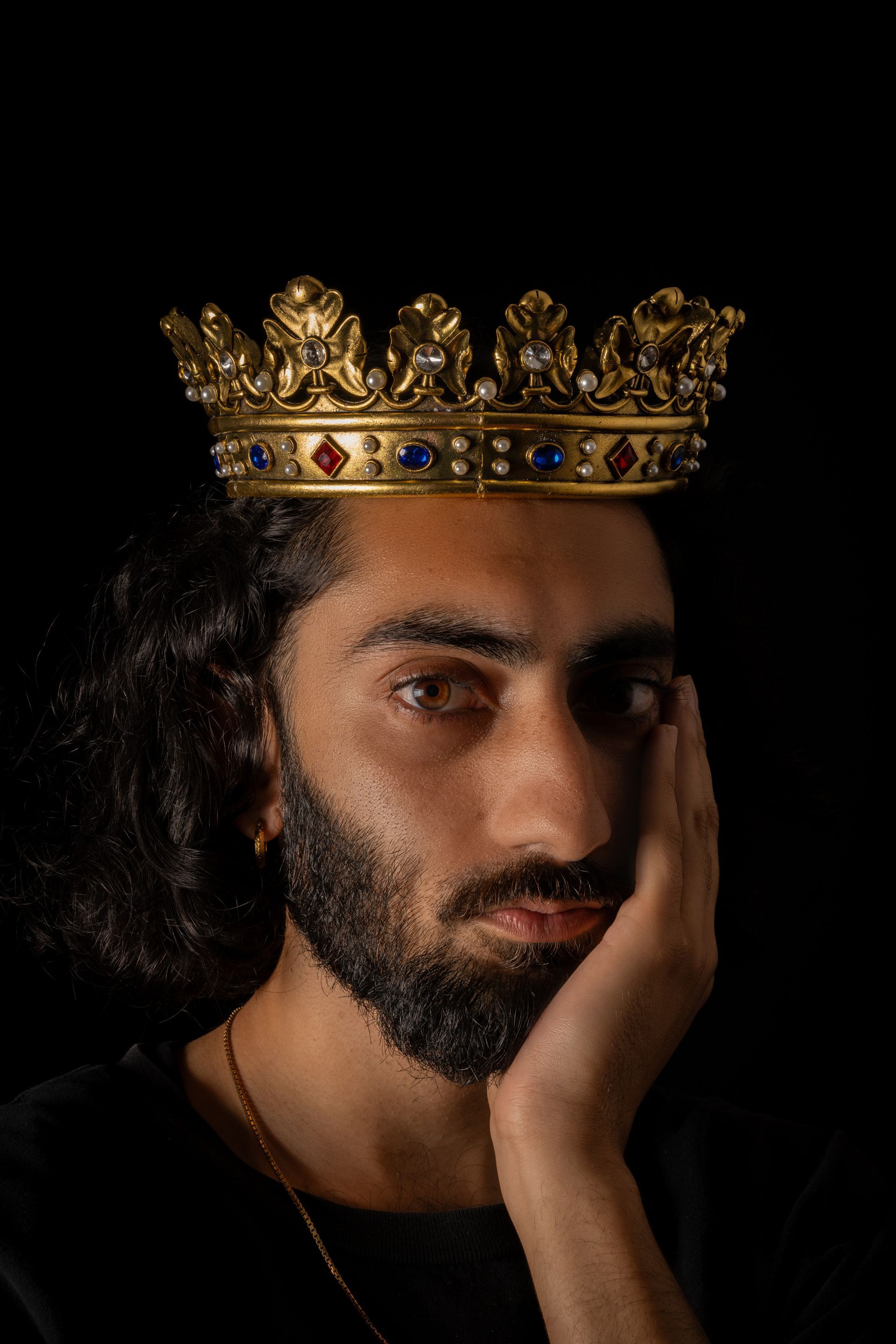 Man with crown, holds face, dark background.