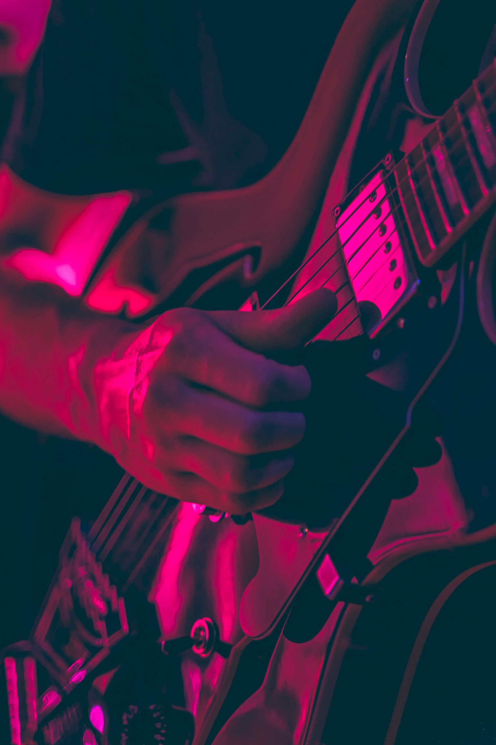 A person's hand plays an electric guitar with a pink and black color scheme.