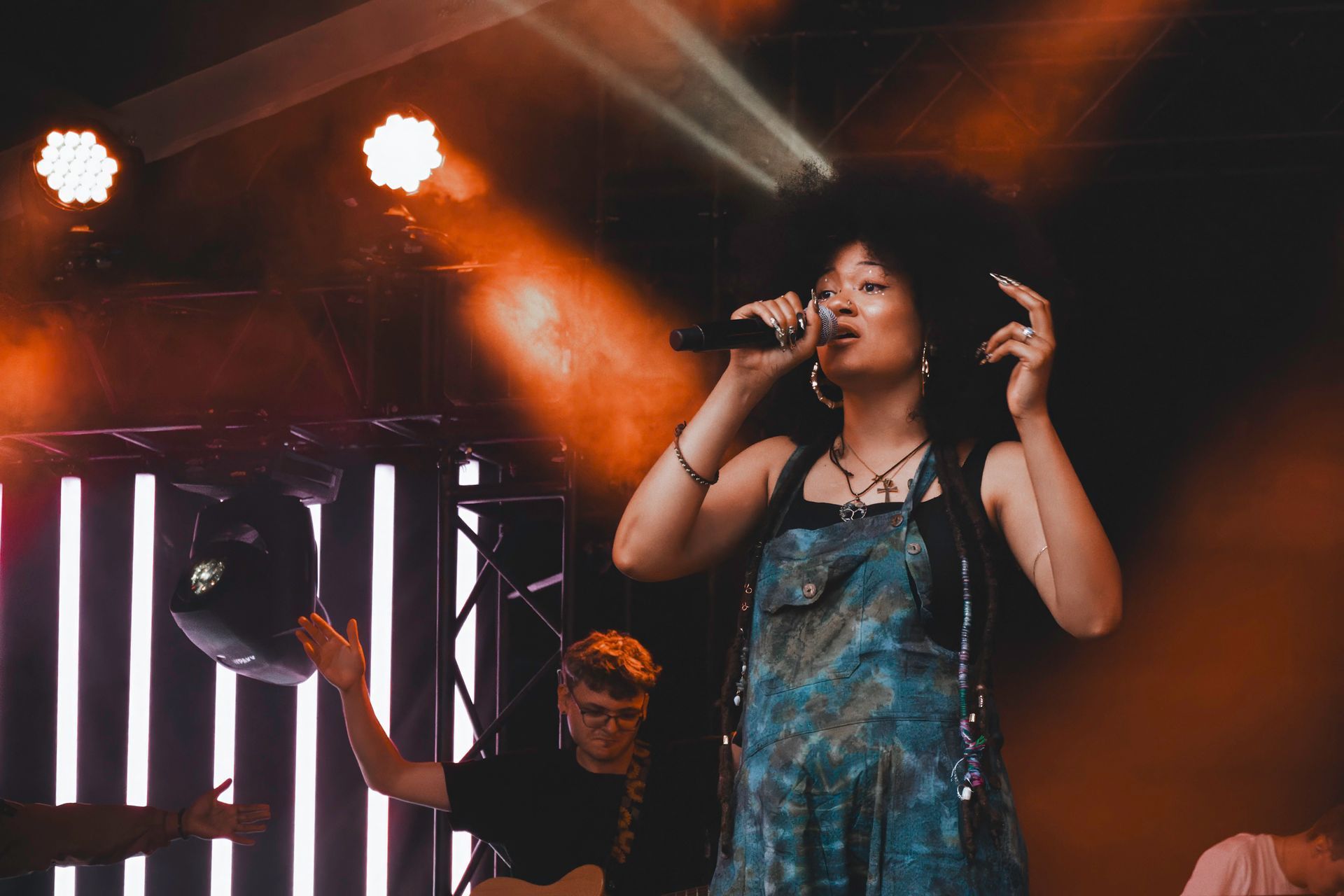 Singer with large afro performing on stage with band, orange lights.