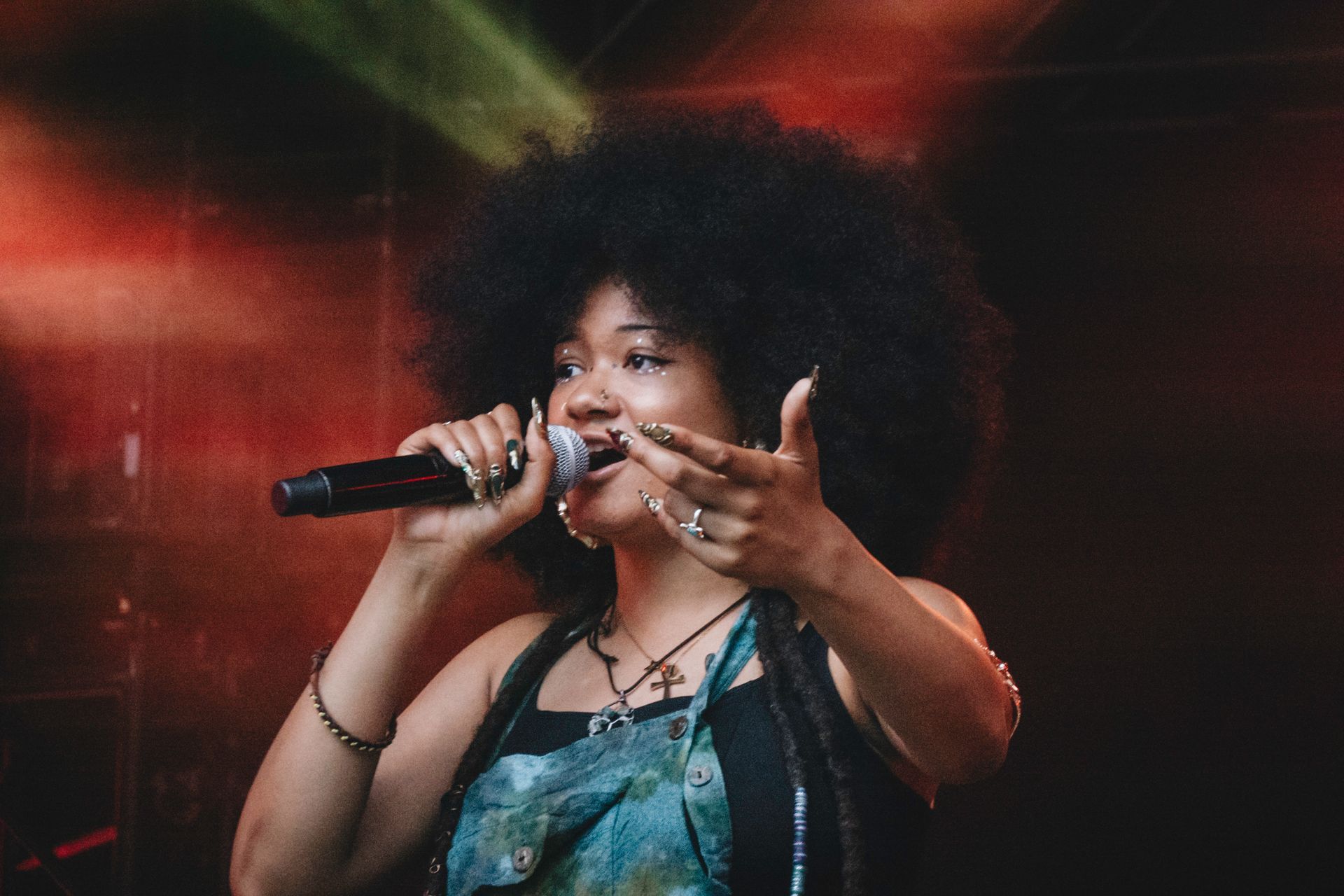 Woman with large afro sings into a microphone, gesturing with one hand on stage.