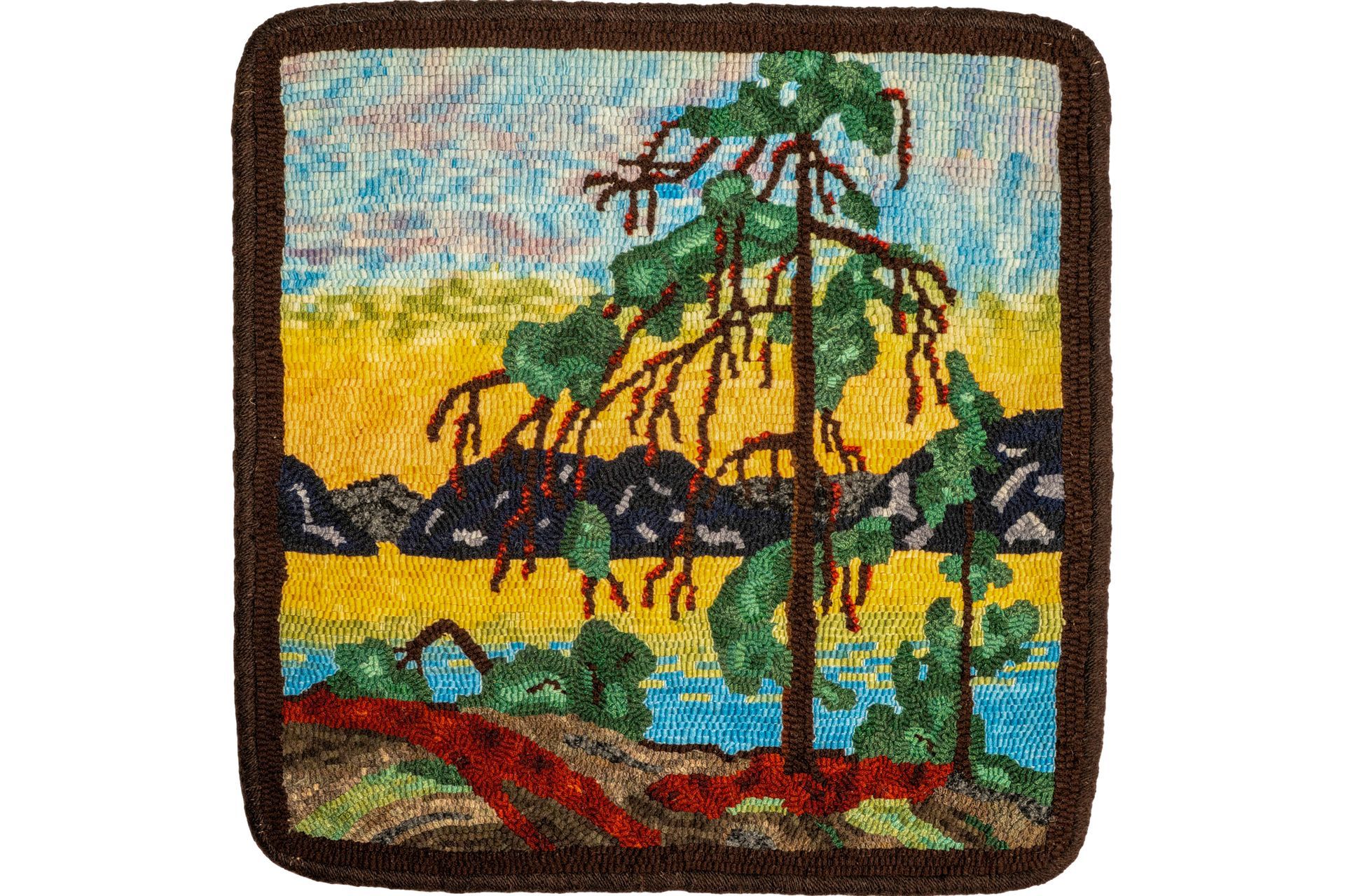 Rug with a landscape of a tree, water, and mountains, in various colors.