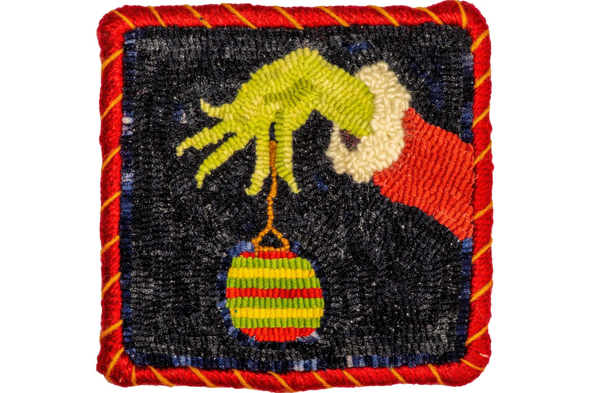 The Grinch's green hand holding a striped Christmas ornament; black, textured background; red and gold braided border.