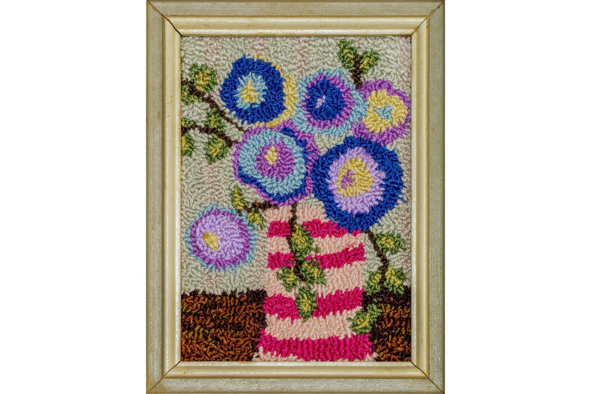 Needlepoint of flowers in vase, framed. Blue, purple, and yellow blooms, striped vase, neutral background.