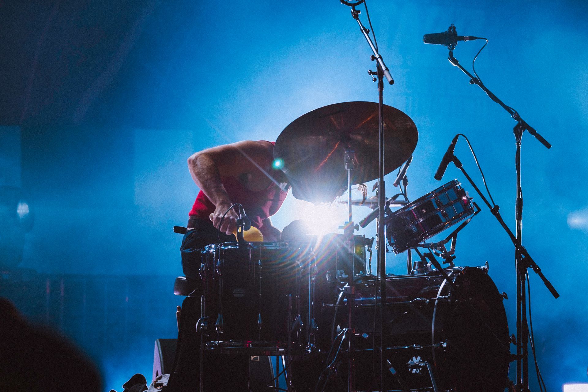 Drummer playing a drum set on a stage lit with blue lights.