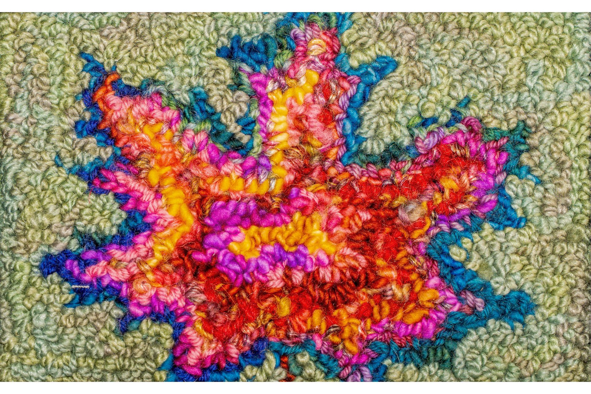 Colorful, textured textile art. A vibrant maple leaf design in red, orange, pink, and yellow. A blue outline against a green background.