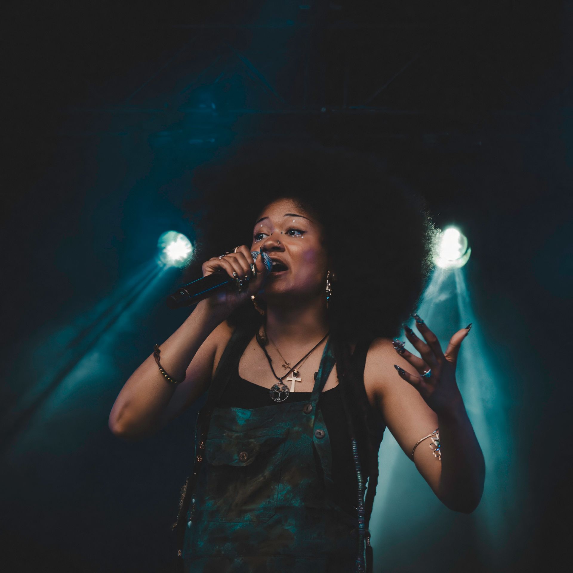 Woman with large afro sings into a microphone on stage, under bright spotlights.
