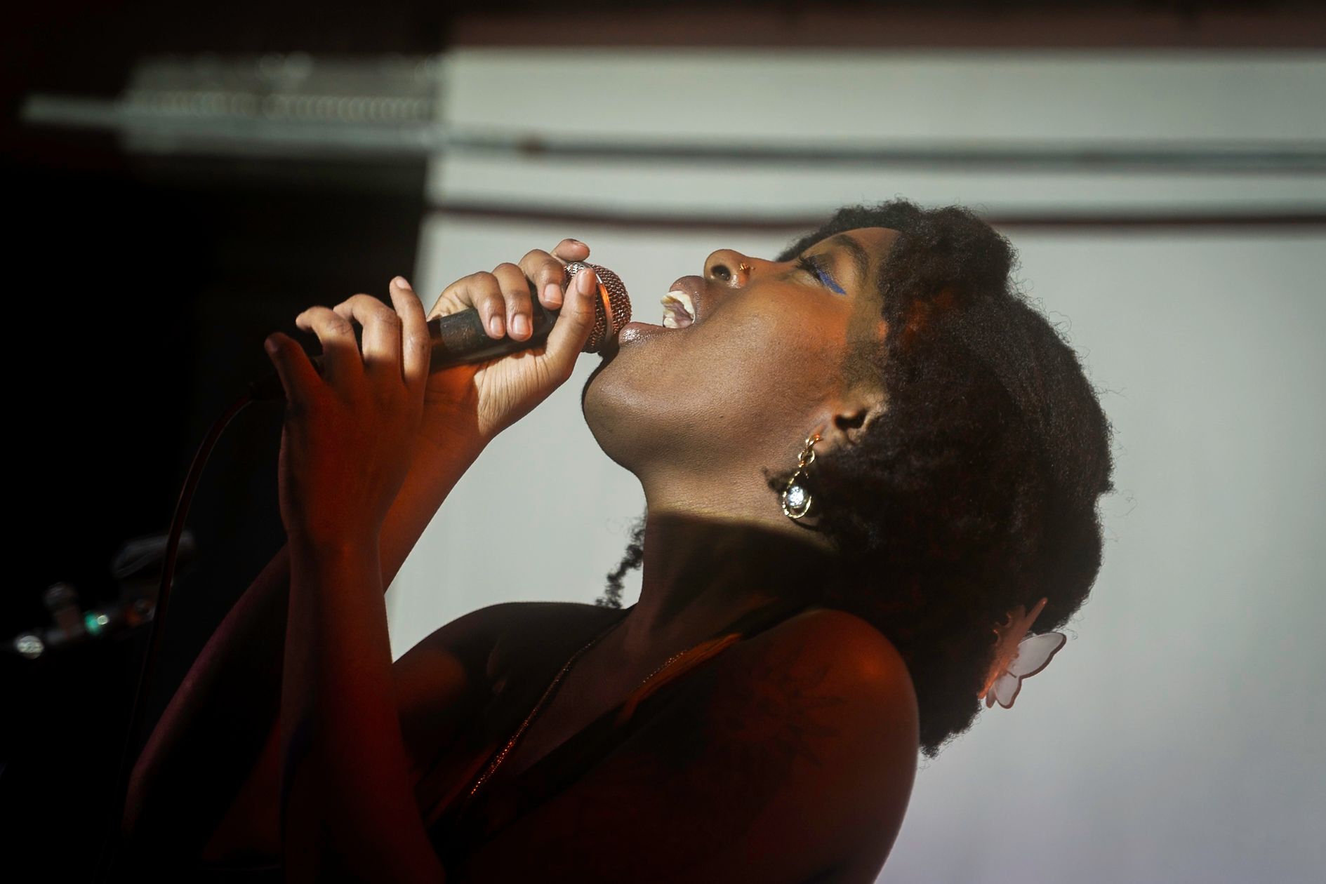 Woman singing into a microphone, head tilted back, mouth open, dark setting.
