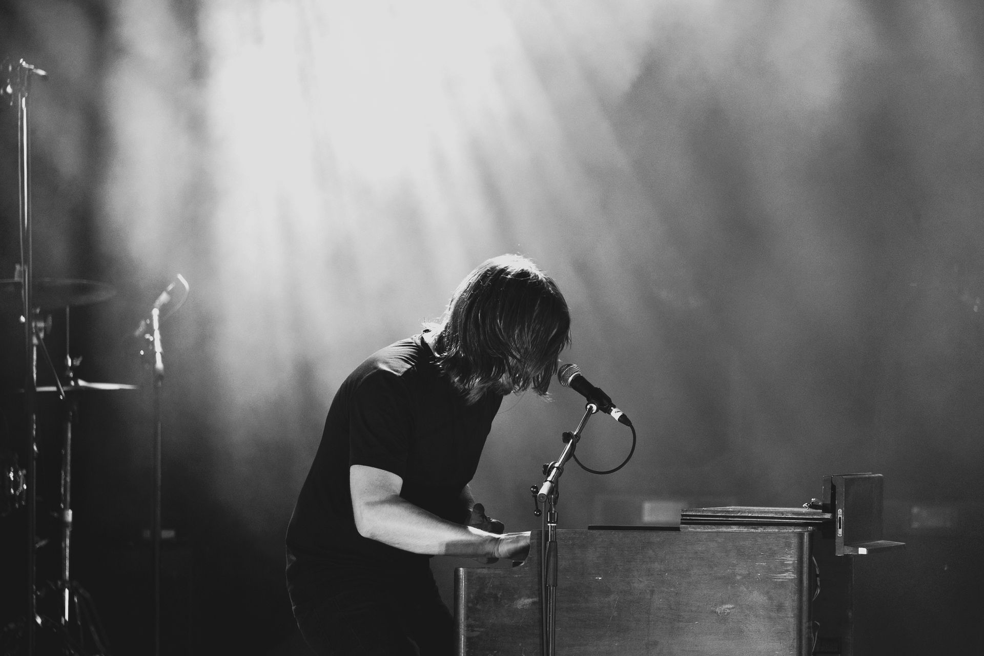 Keyboardist on stage, backlit by stage lights, playing keys with focus.