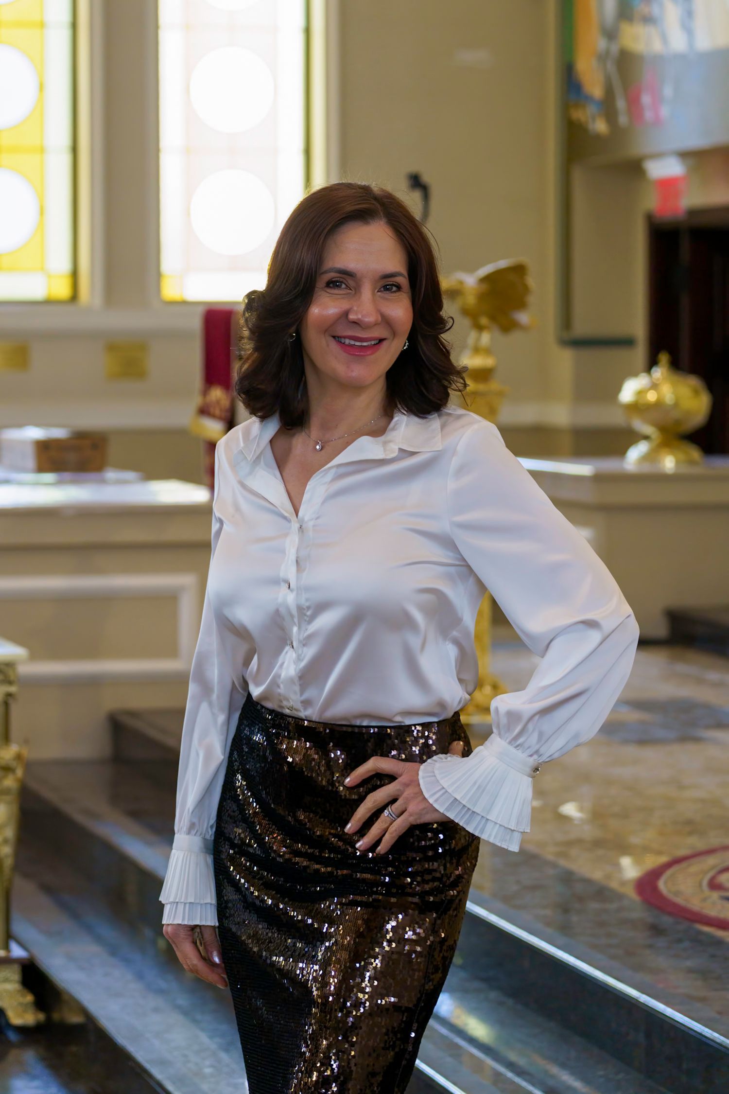 Woman in white shirt and sequined skirt poses in a church.