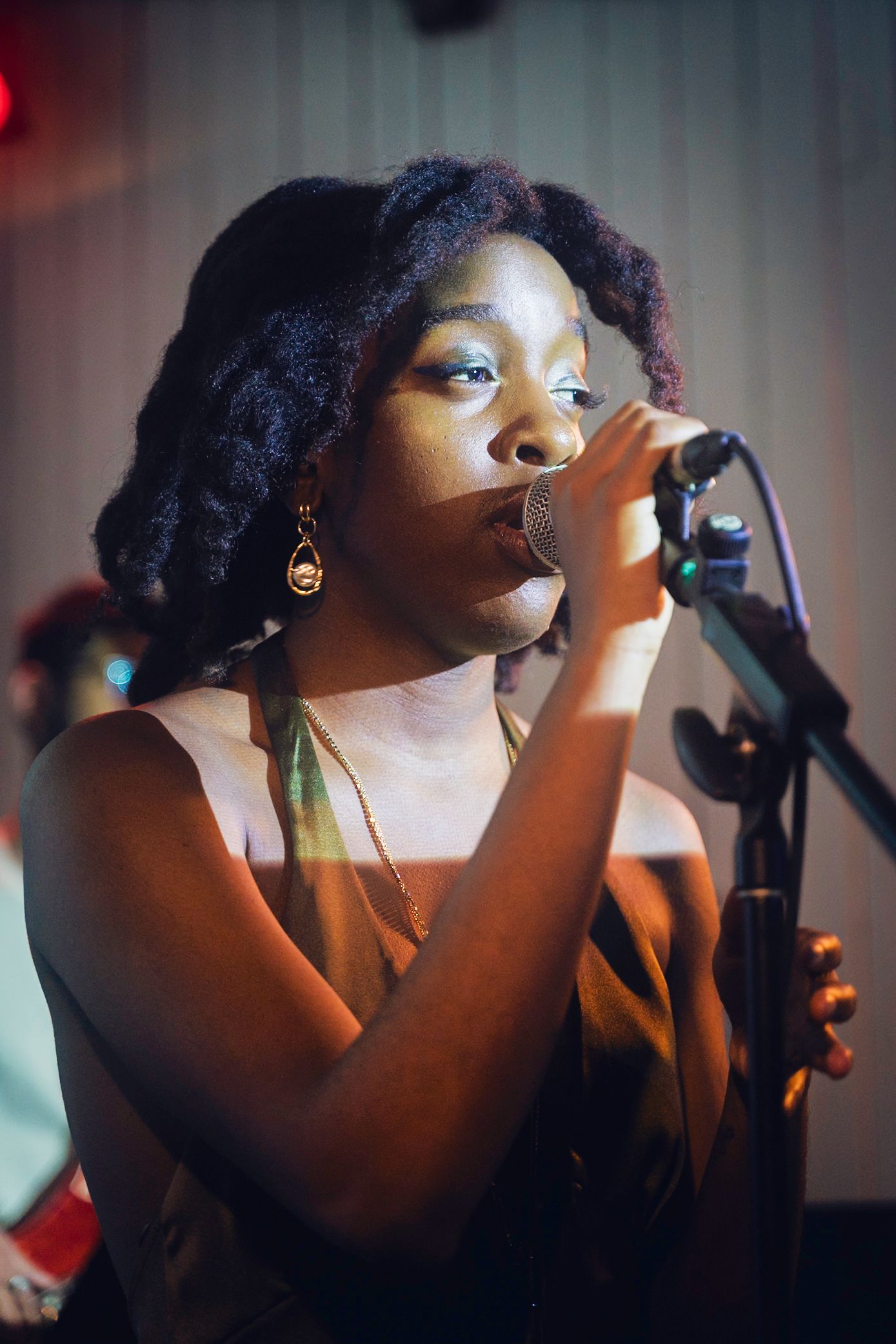 Woman singing into a microphone on stage, wearing a brown top.