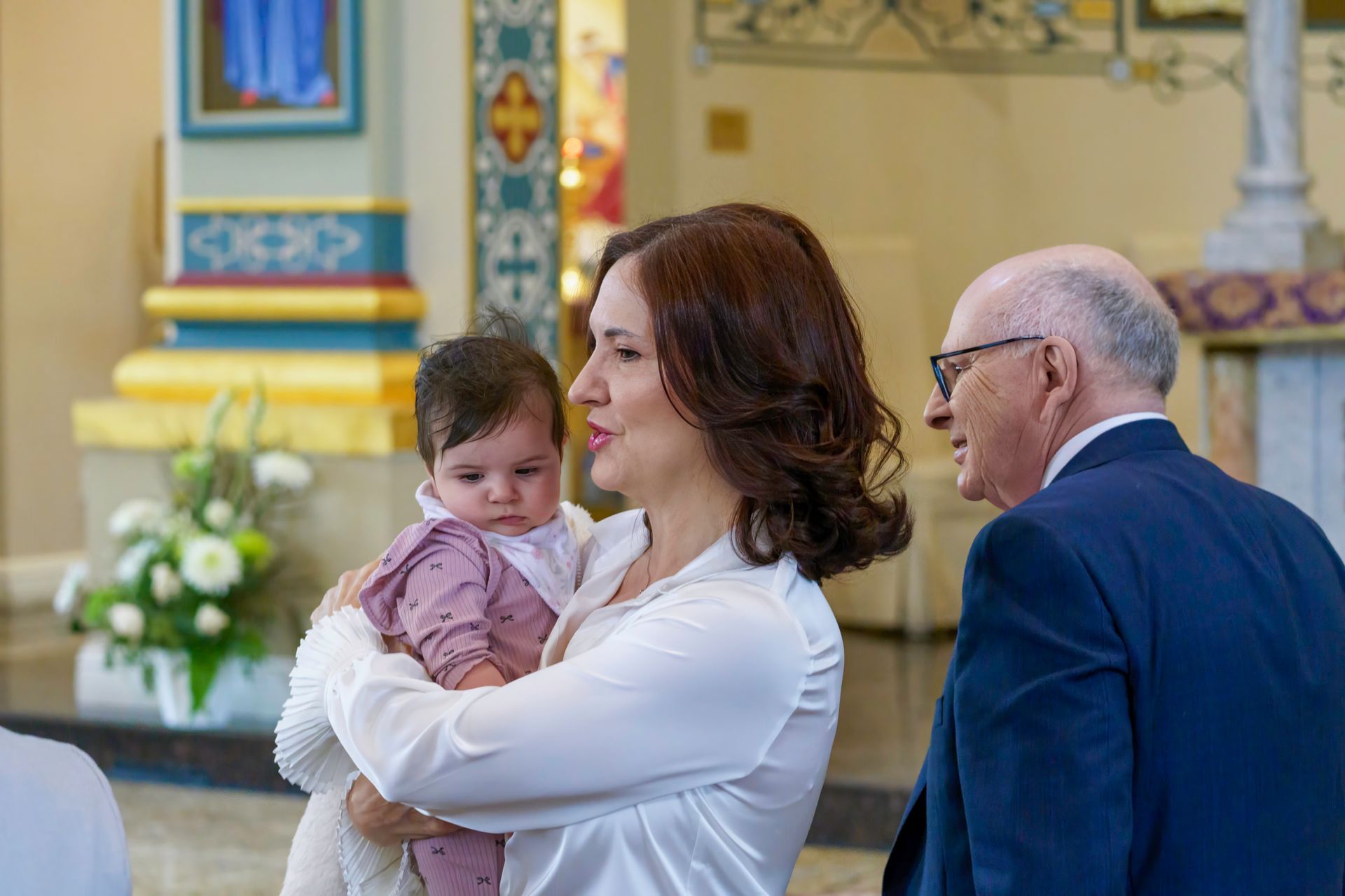 Woman holding a baby, standing in a church near a man in a suit.