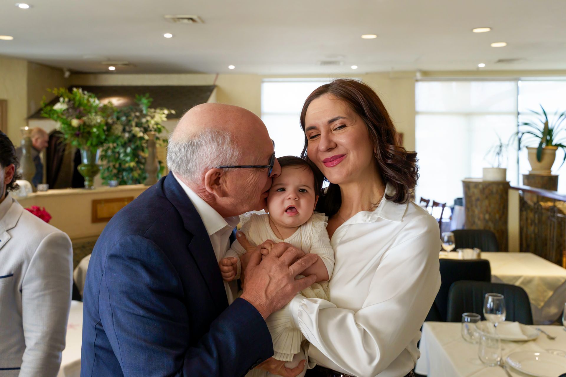 Man kissing a baby held by a woman in a restaurant.