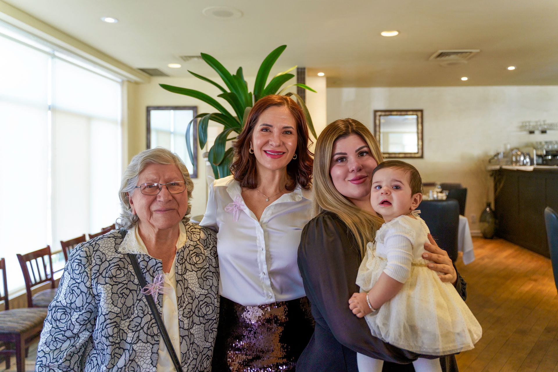Four women posing together in a restaurant: older woman, middle-aged woman, young woman holding a baby.