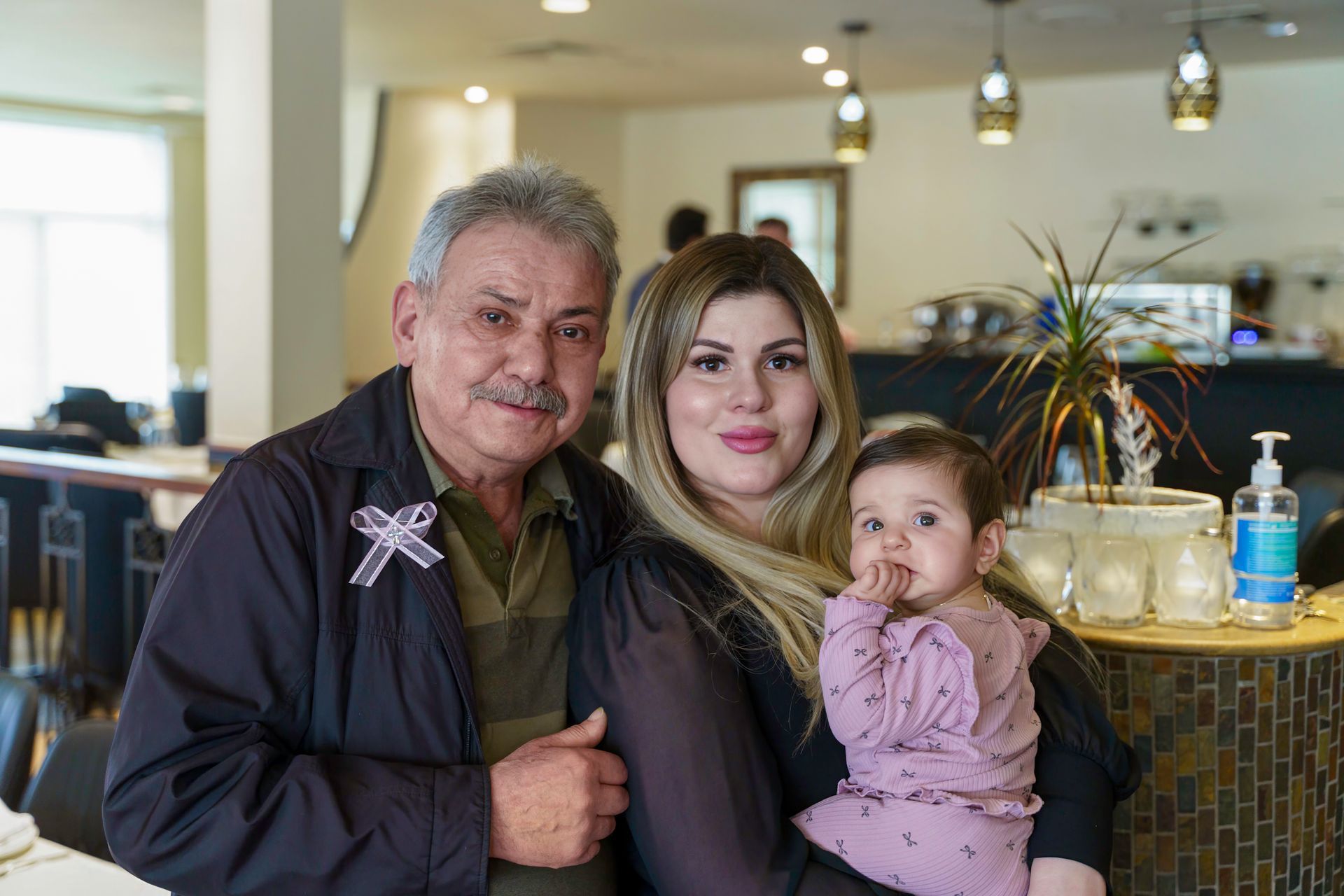 Family in restaurant, grandfather, woman, and baby. Smiling, near table, with hand sanitizer.