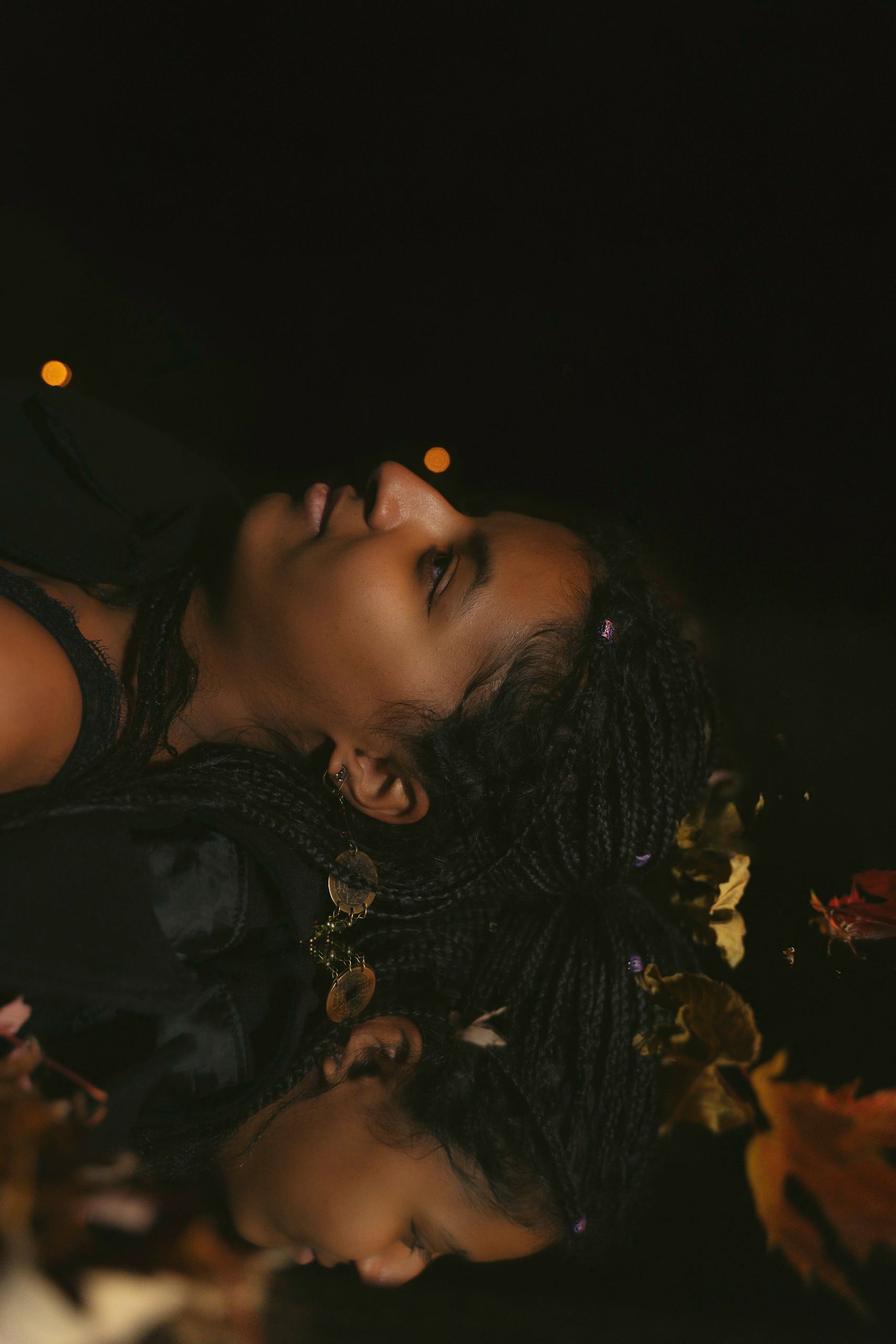 Woman with closed eyes floats in dark water, hair and leaves around her.