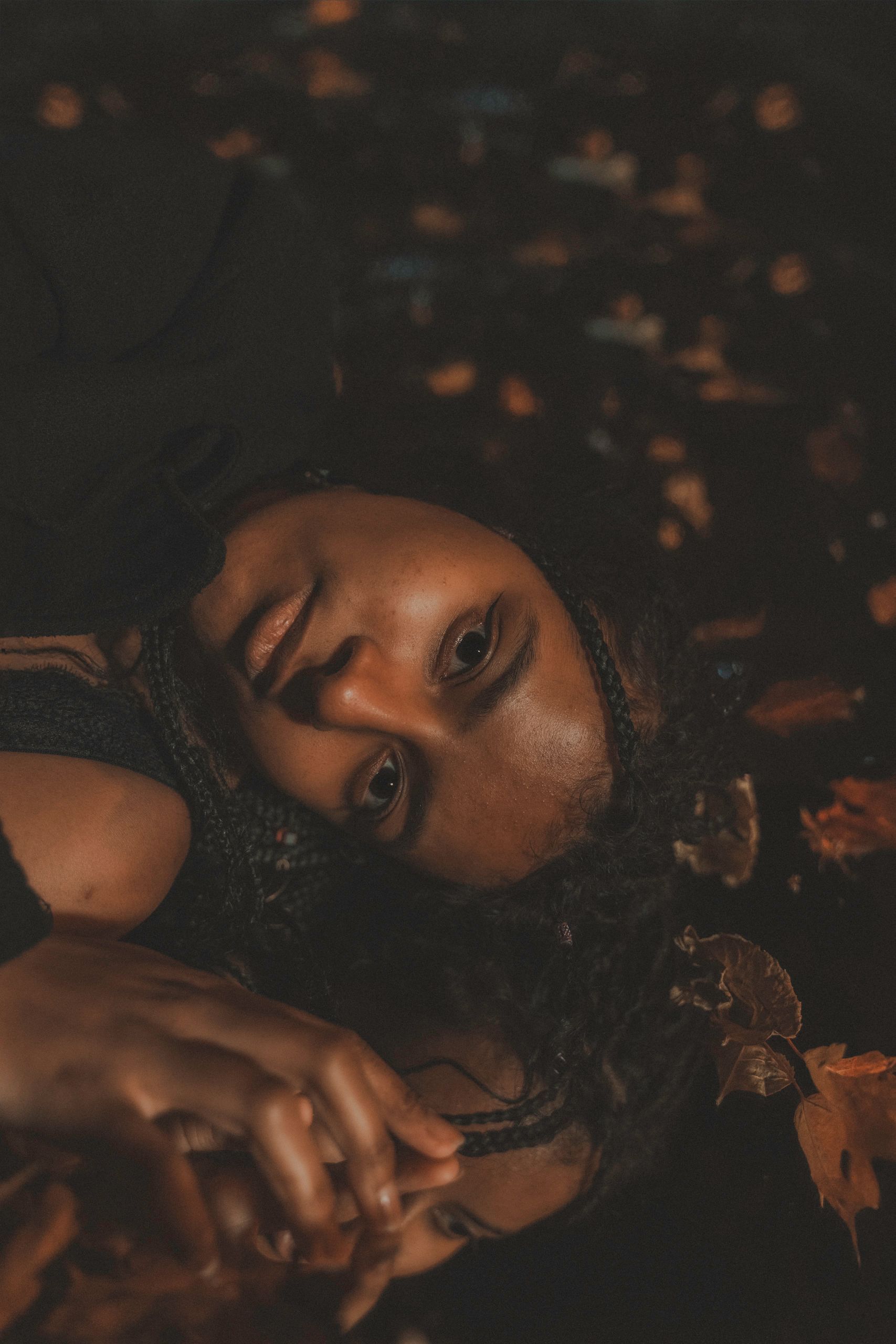 Person's face reflecting in water. Leaves scattered around, warm lighting, looking up.