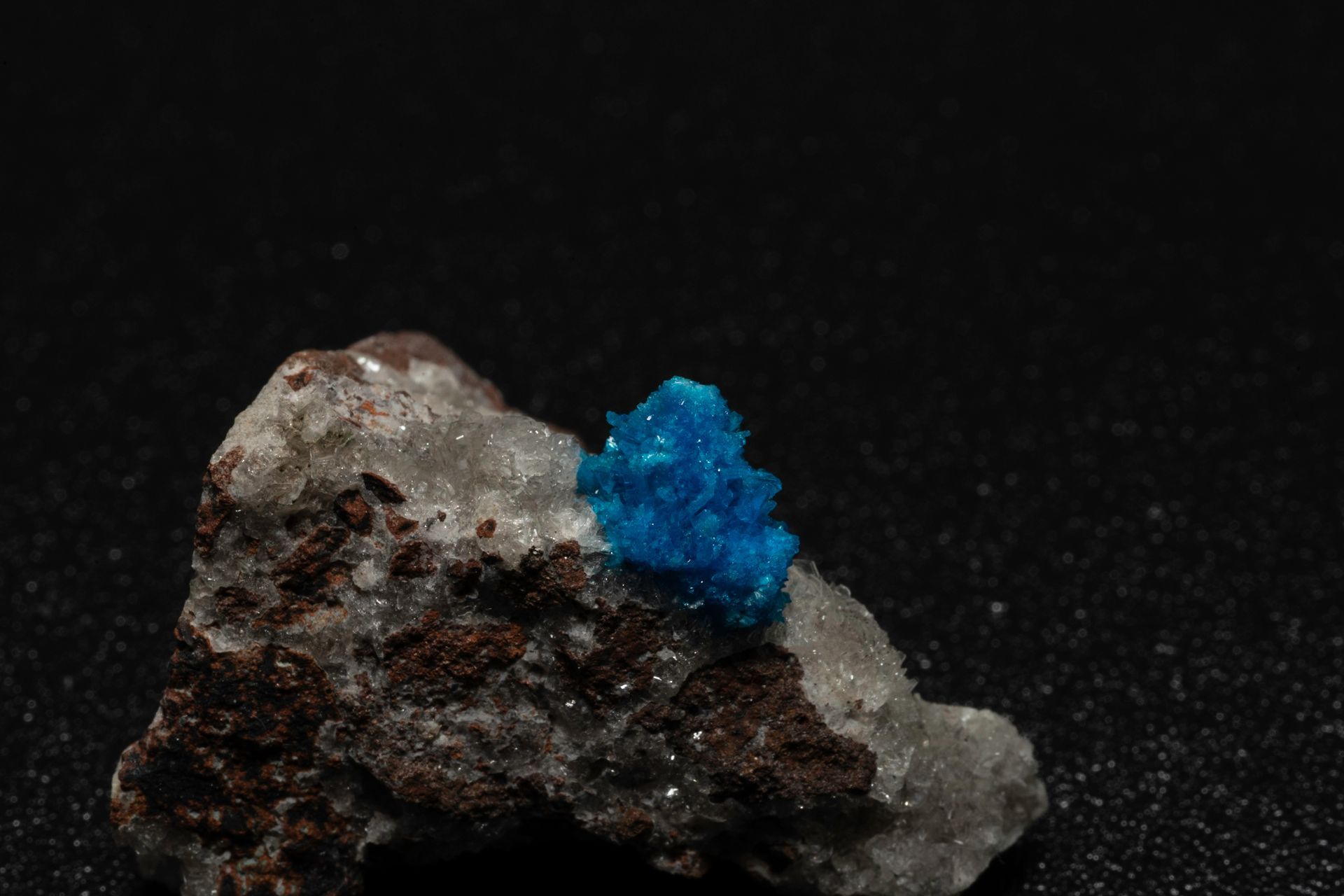 Blue crystal cluster on gray and brown rock, against a black background.