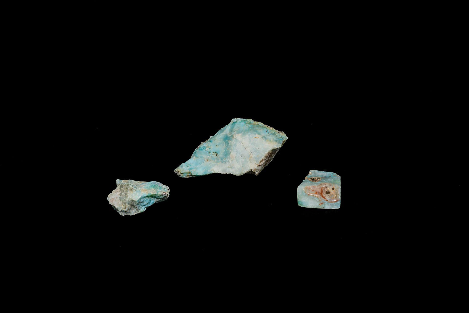 Three pieces of turquoise-colored, fragmented rock against a black background.
