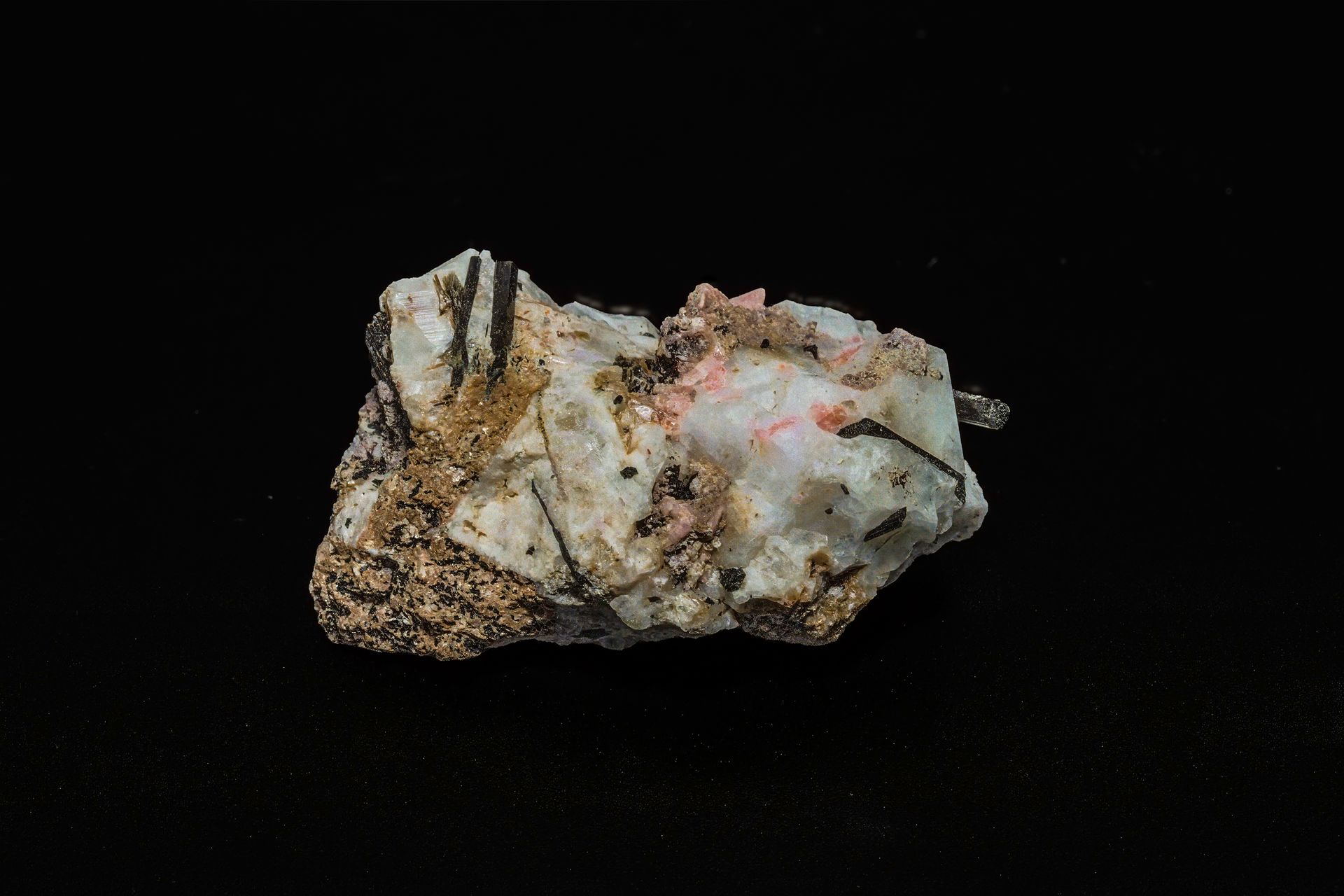 Mineral sample with white, tan, and black components on a black background.