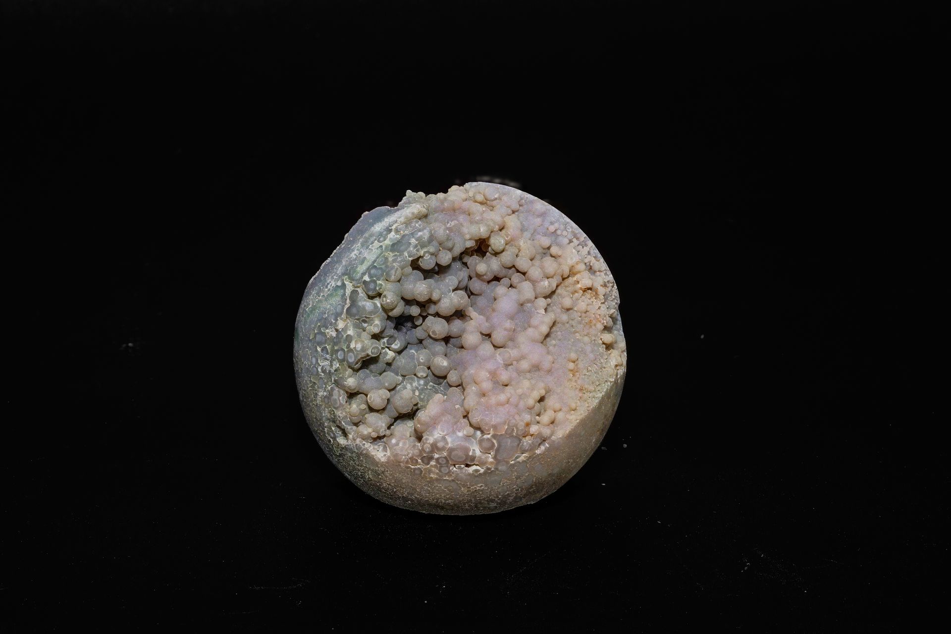 Round, textured, pale-purple rock against a black backdrop, with a rough, granular surface.